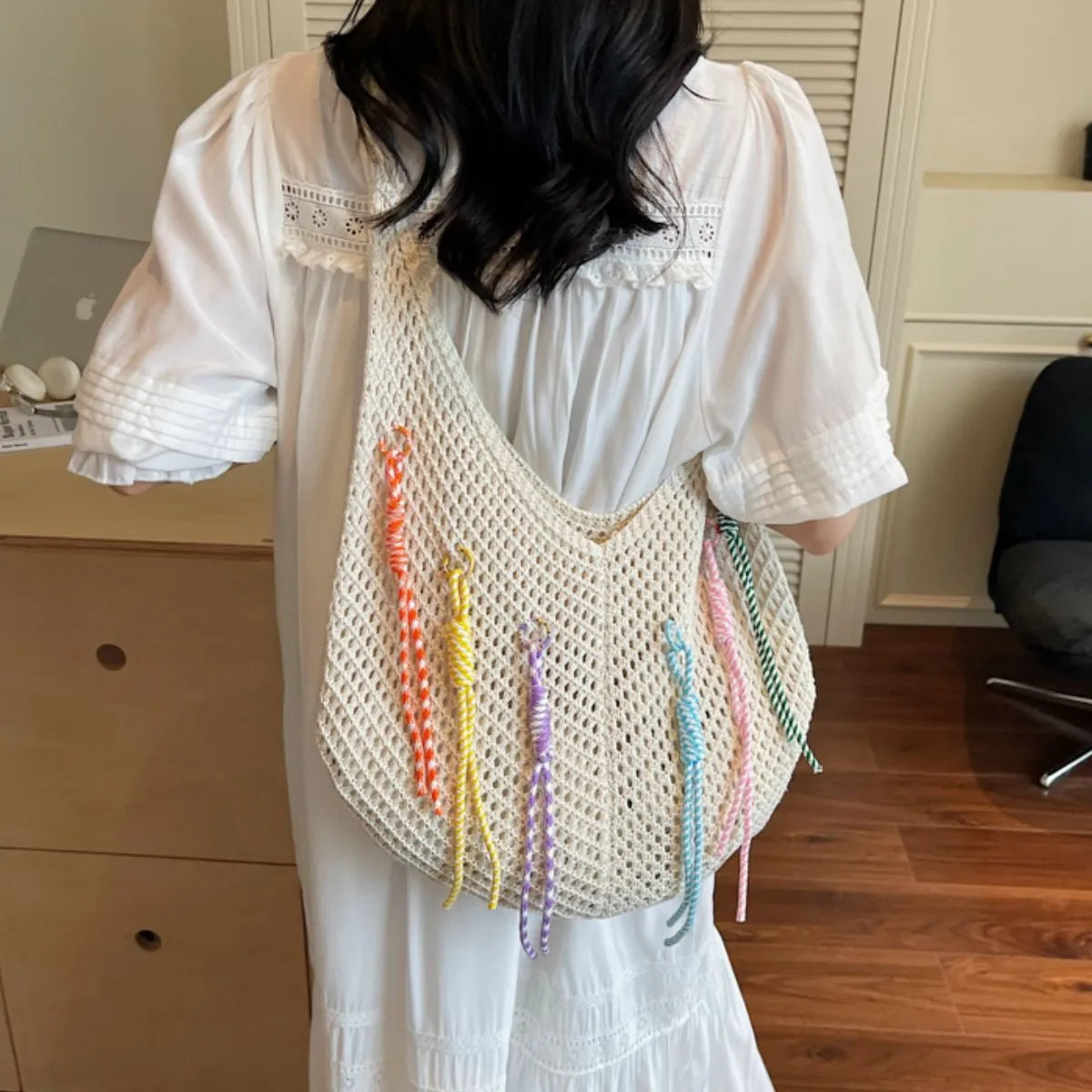 Person wearing a white crochet bag with colorful tassels indoors.