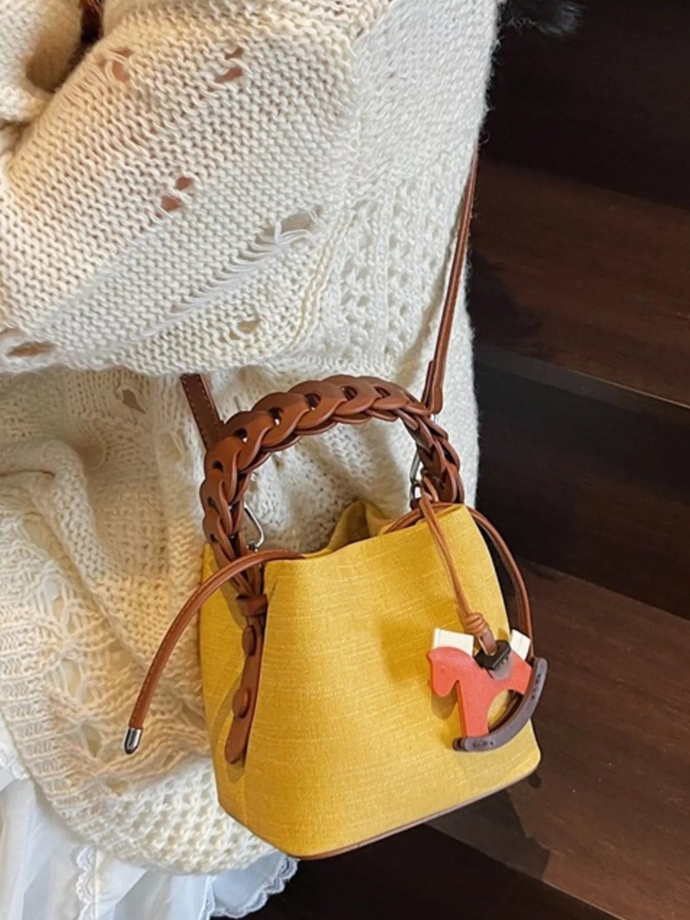 Yellow handbag with brown handle and decorative charm on a textured surface
