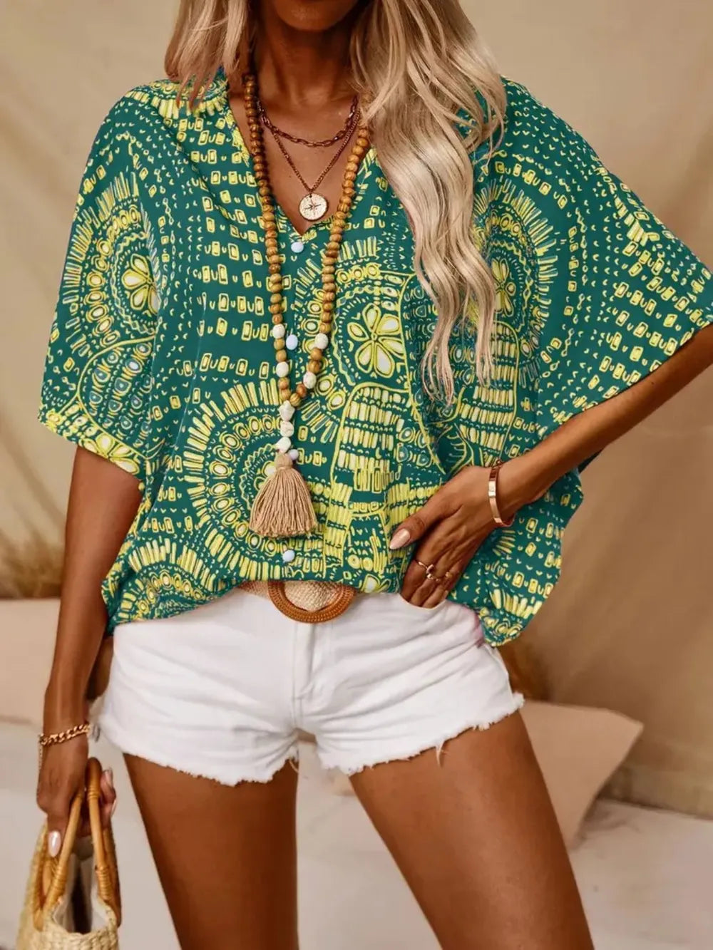 Woman wearing a green and yellow patterned top with white shorts, standing against a neutral background.