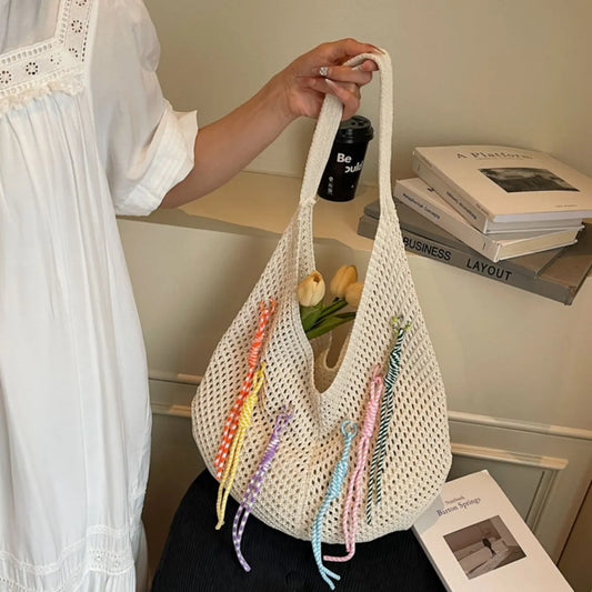 Person holding a white mesh bag with colorful drawstrings in a casual setting.