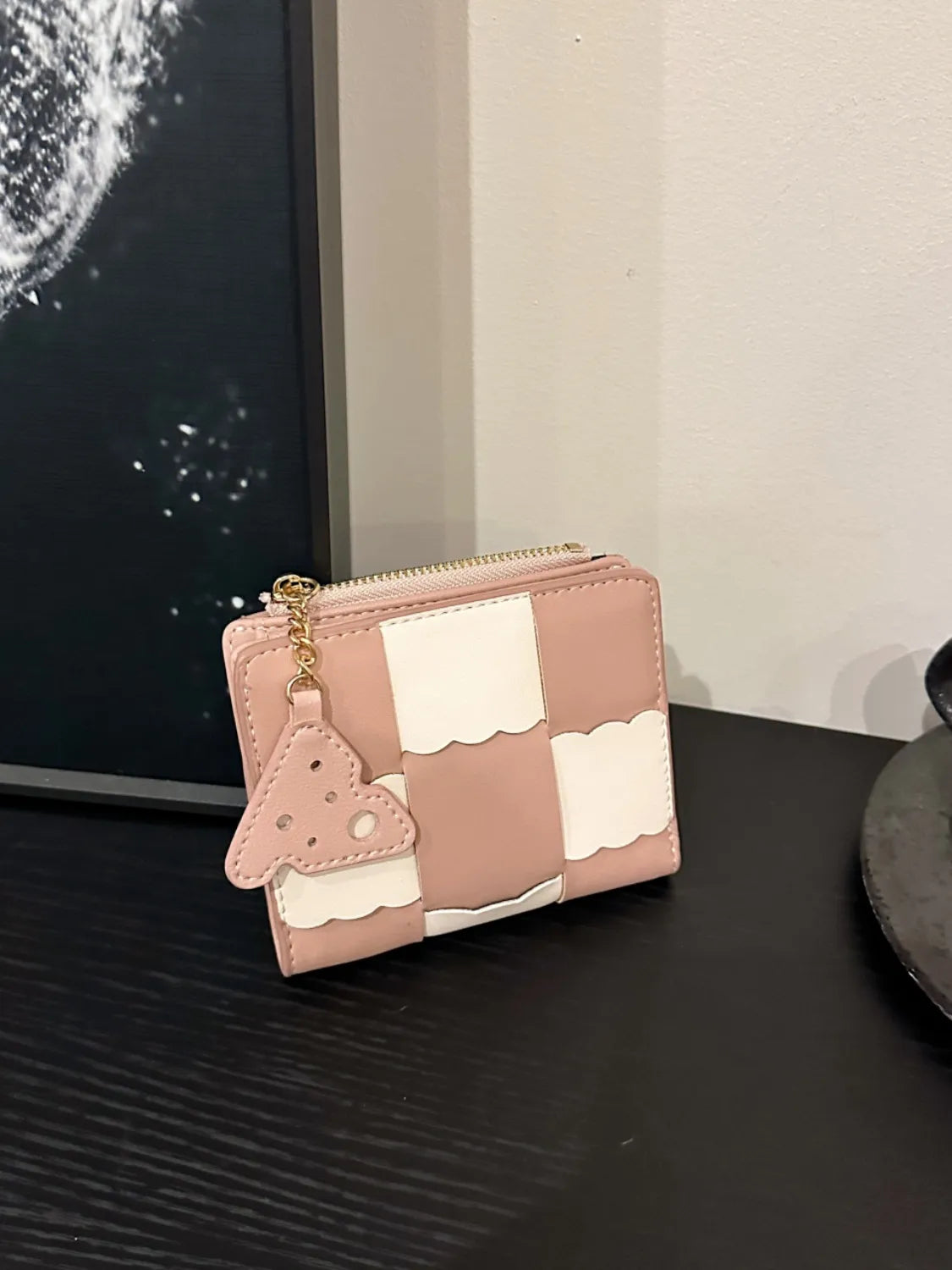 Pink and white wallet with a small bag charm on a dark surface.