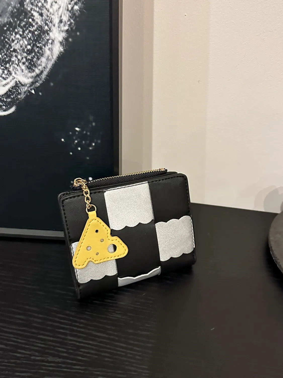 Black and white checkered wallet with a yellow heart charm on a dark surface.