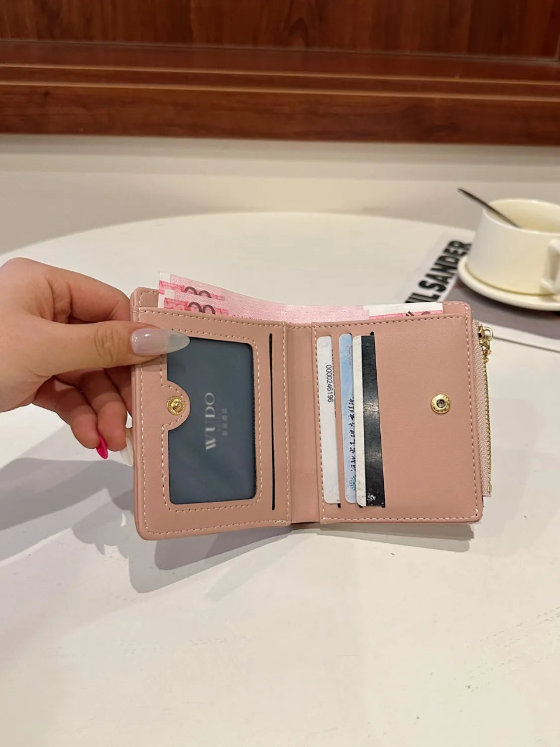 Pink wallet with card slots held by a hand on a white surface.