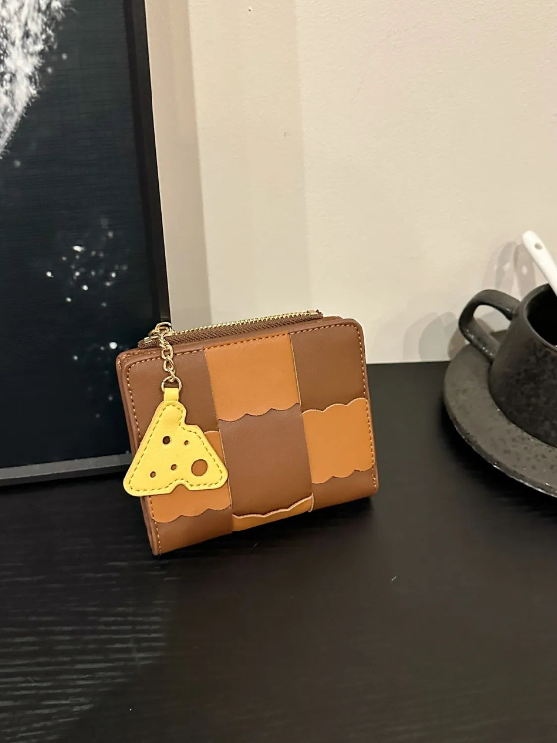 Brown patchwork wallet with a yellow triangle charm on a dark surface.