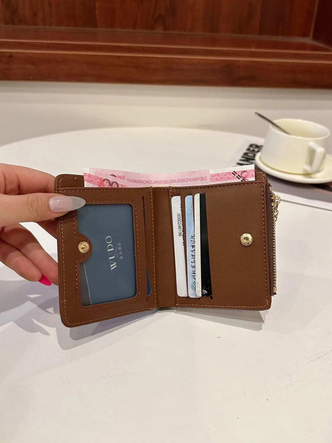 Brown wallet with visible brand name held by a hand on a white surface.