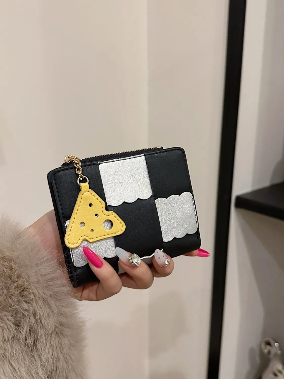 Black and white patterned wallet with a yellow triangle charm held by a person.