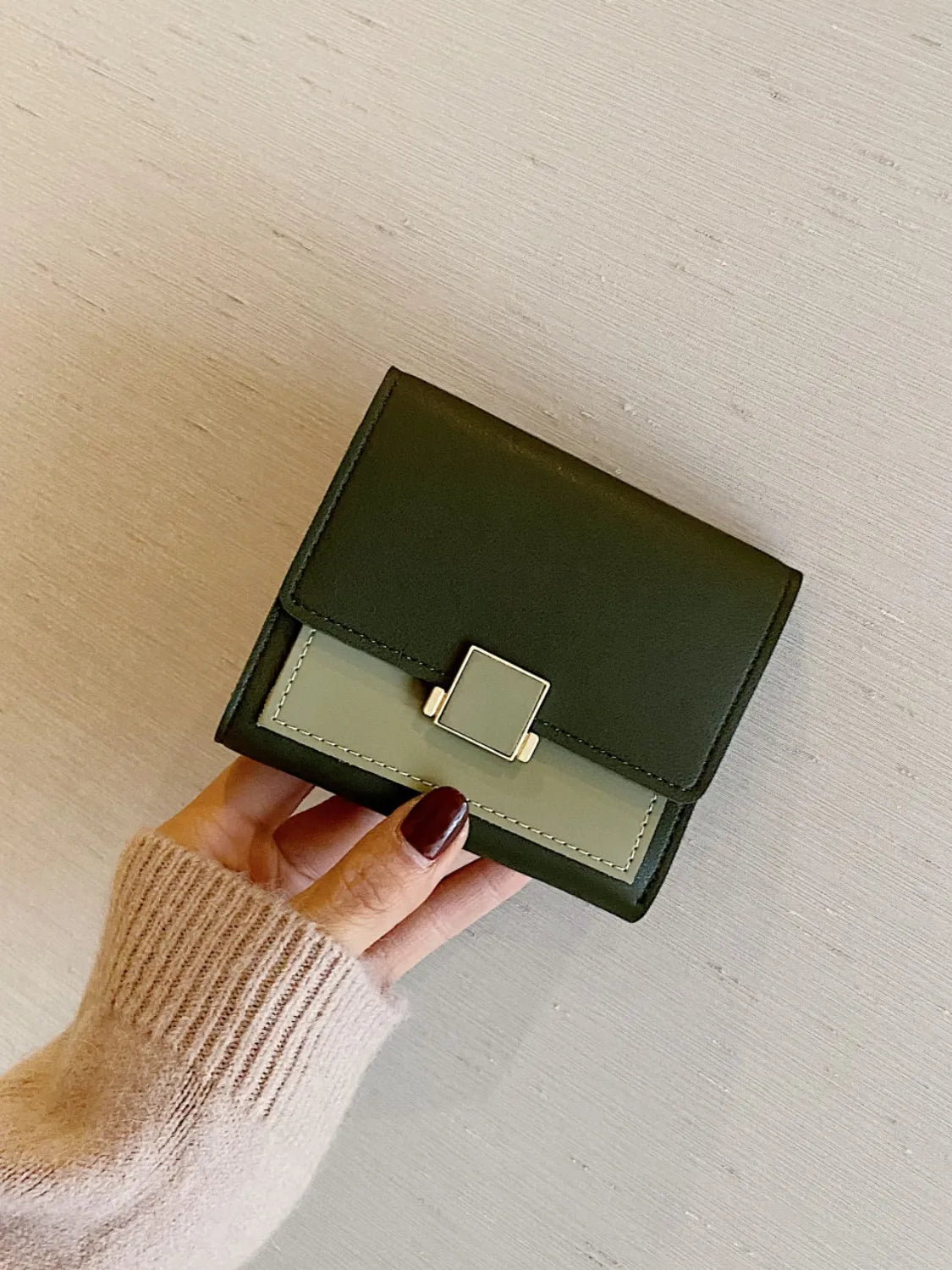 Hand holding a green wallet against a neutral background