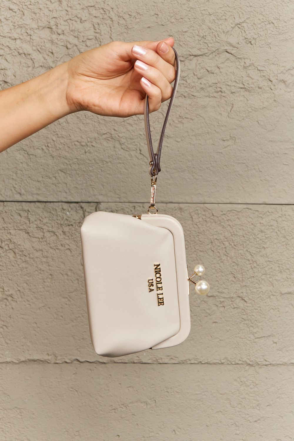 Beige pouch with a strap held by a hand against a beige wall