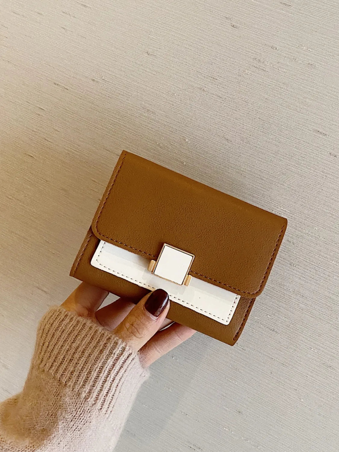 Brown wallet with a white accent held by a hand on a light wooden surface