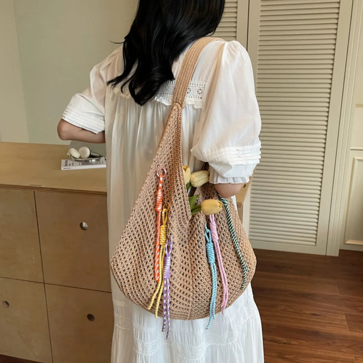 Person wearing a beige woven bag with colorful tassels indoors.