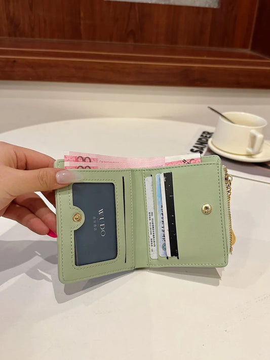 Hand holding a light green wallet with cards and cash on a white surface.