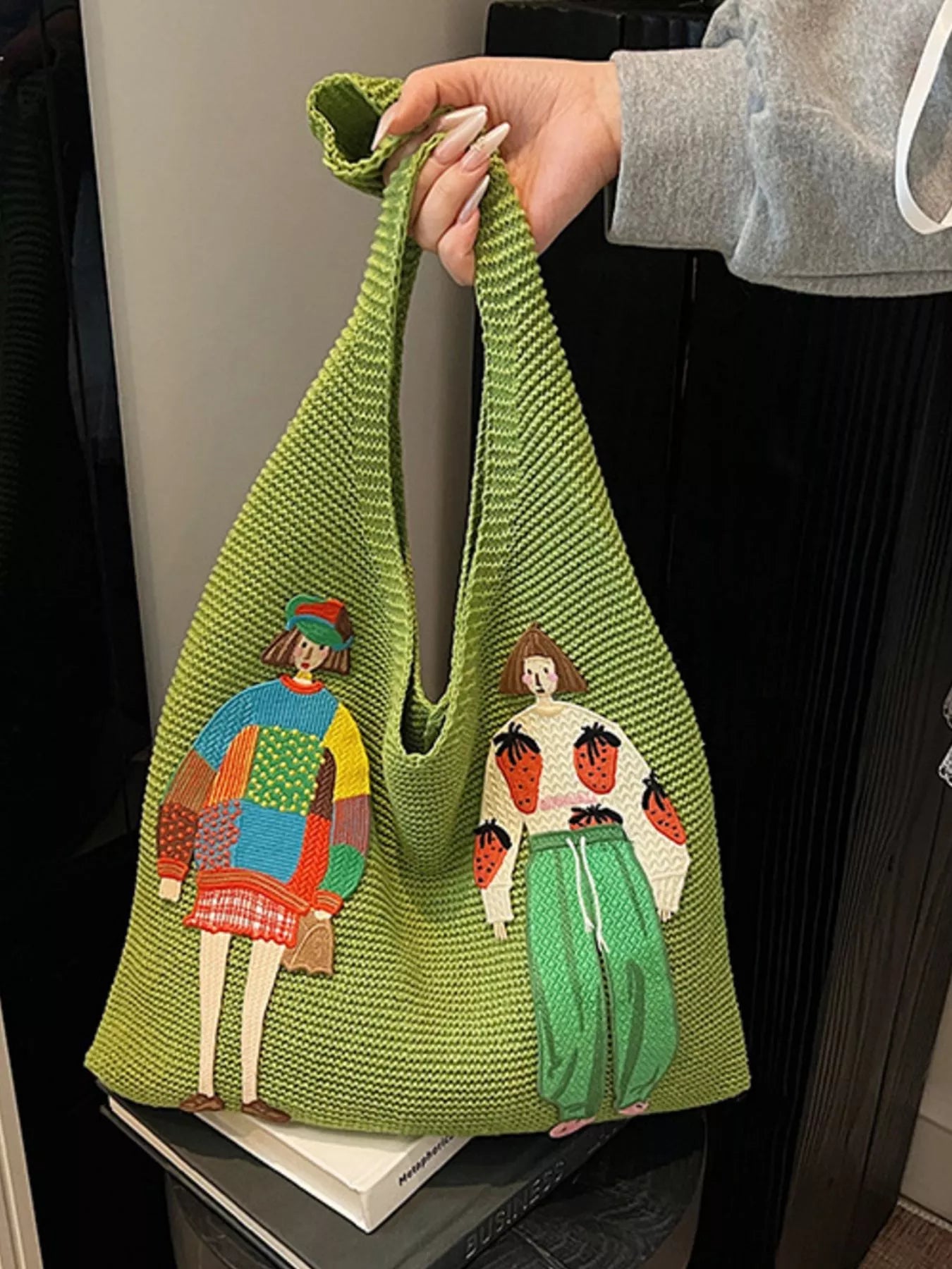 Green woven bag with embroidered characters held by a person