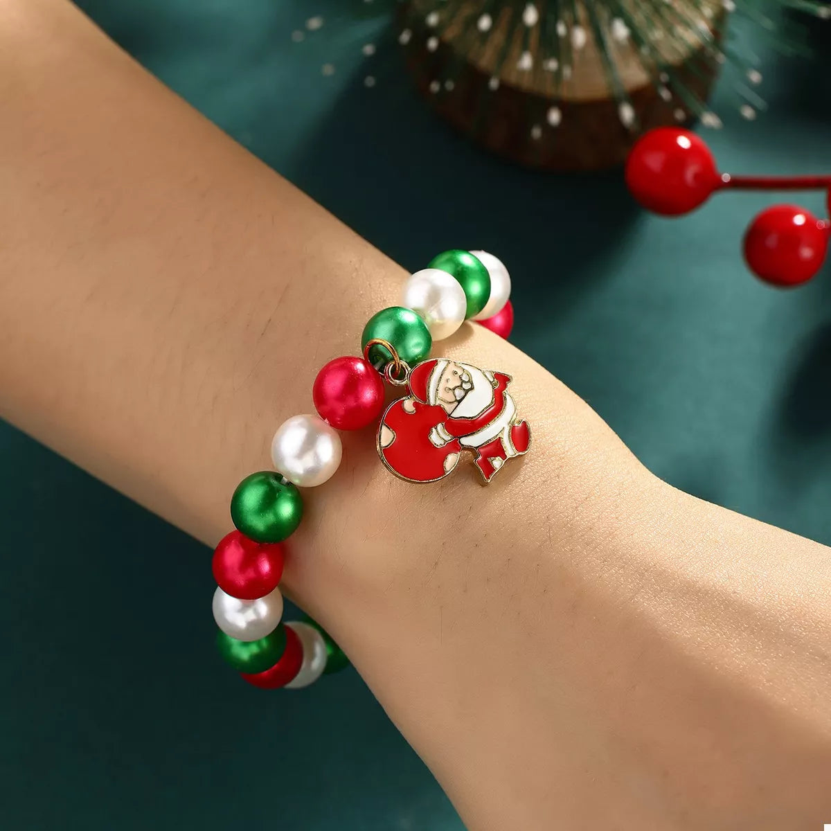 Bracelet with red, green, and white beads and a Santa Claus charm on a wrist against a green background.
