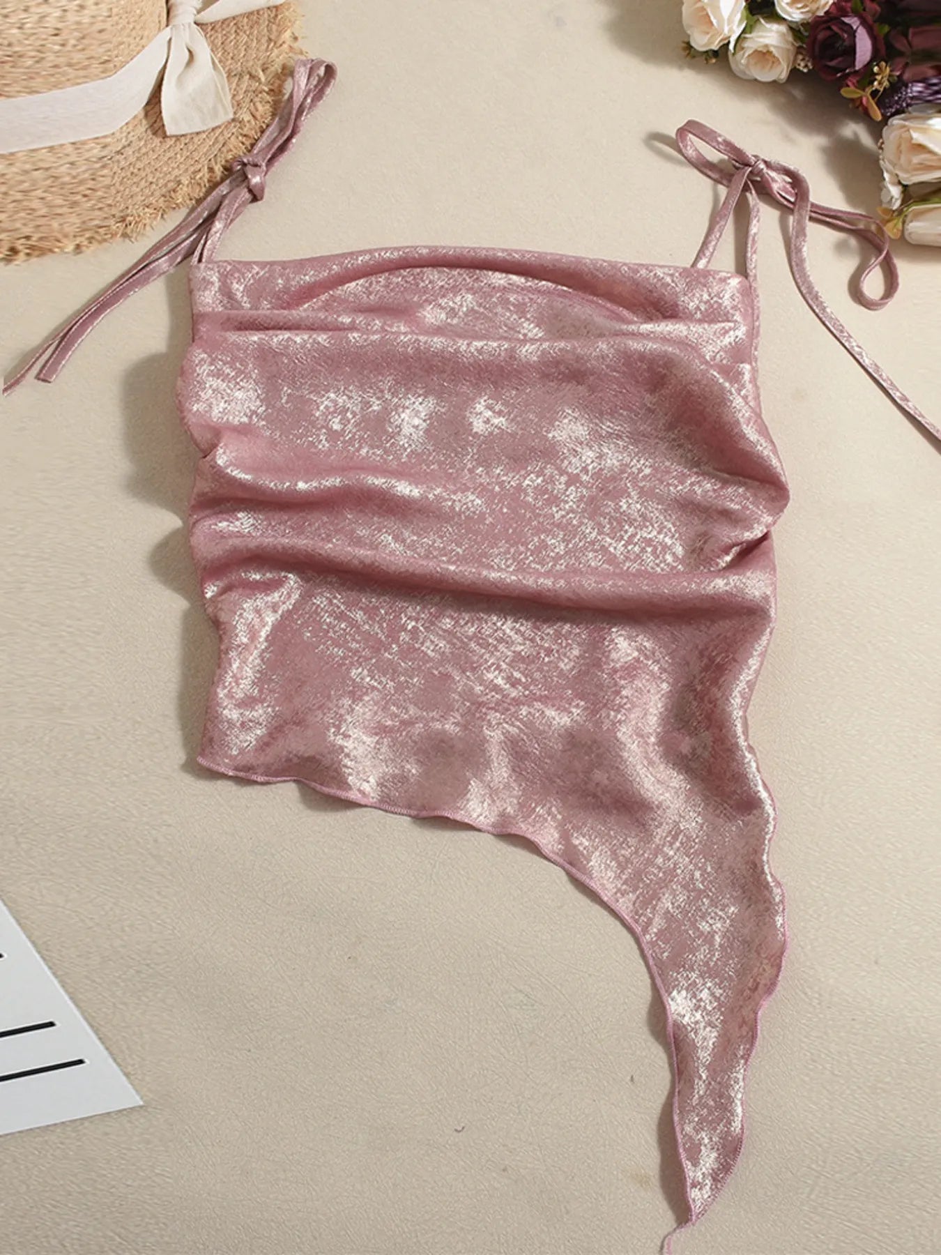 Pink glittery halter top on a beige surface with a straw bag and flowers in the background.