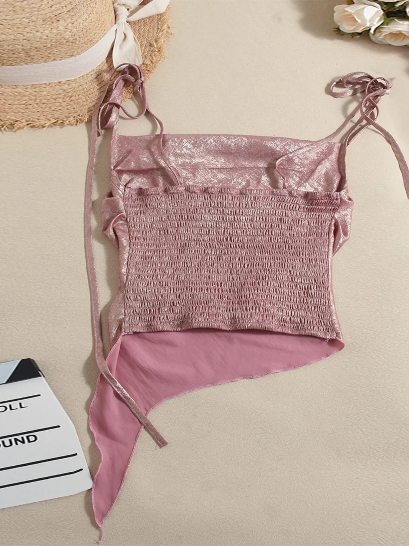 Pink bikini set on a beige surface with a straw bag and flowers in the background