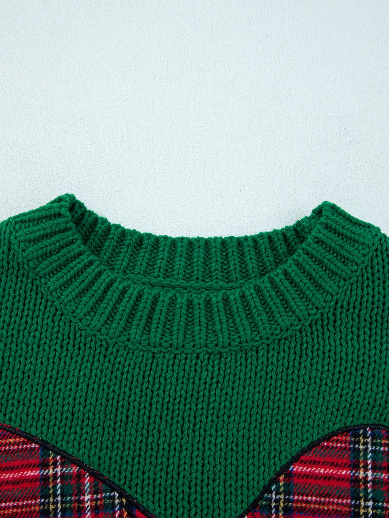 Green knitted sweater with plaid pattern on a light blue background