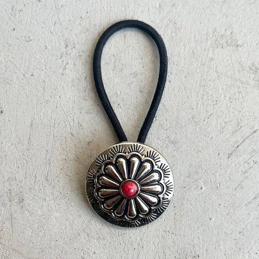 Silver hair tie with a red stone on a light gray background