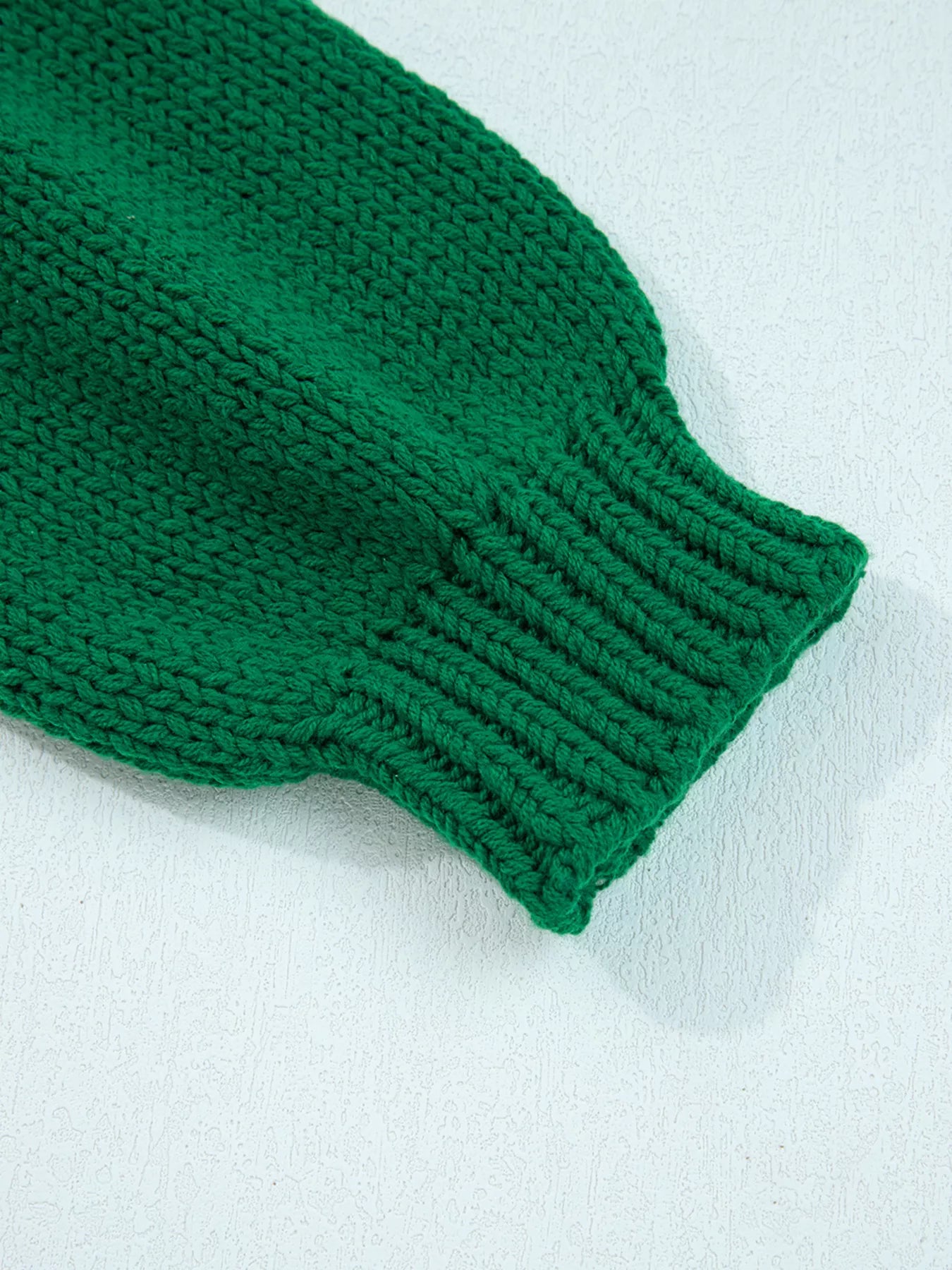 Close-up of a green knitted sweater sleeve on a white background