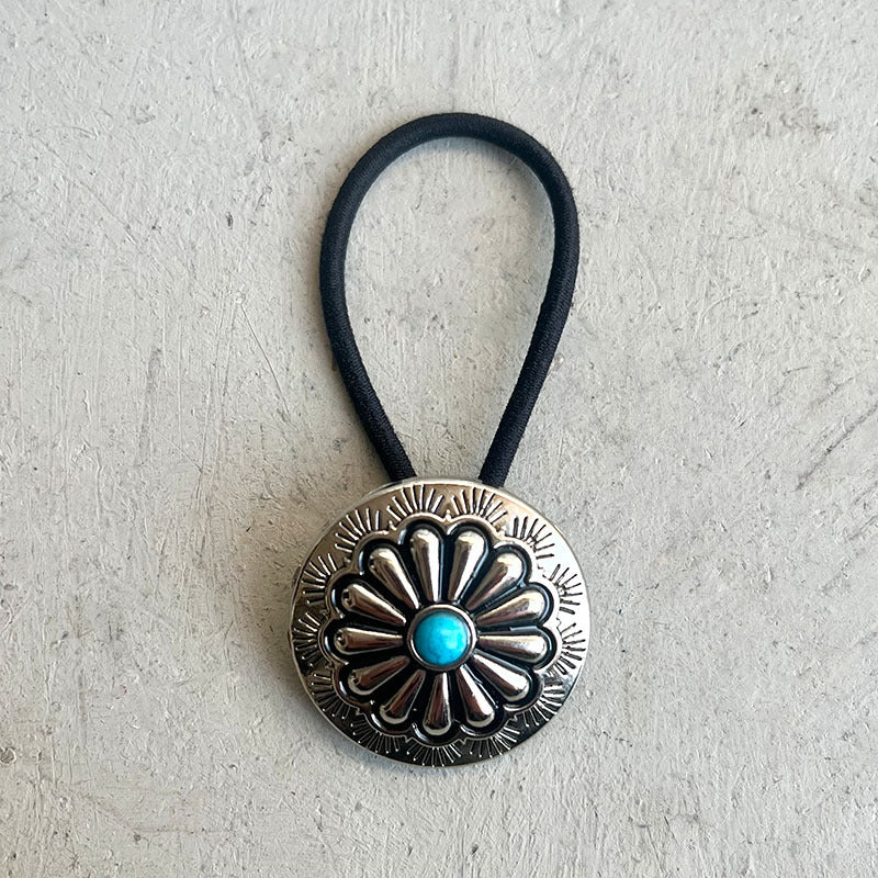 Silver hair tie with floral design and turquoise stone on a textured gray background
