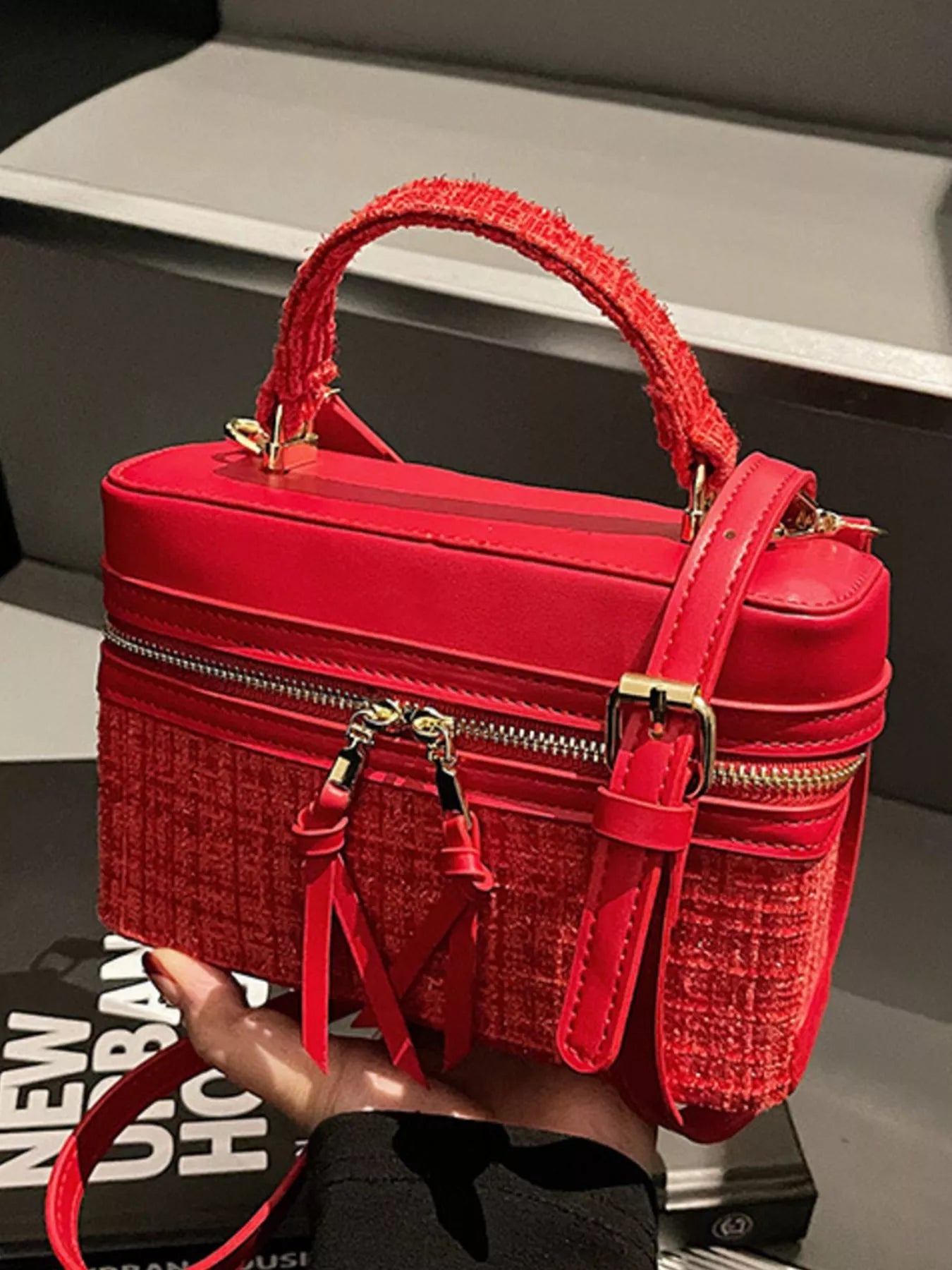 Red handbag with gold accents held by a person, with a blurred background