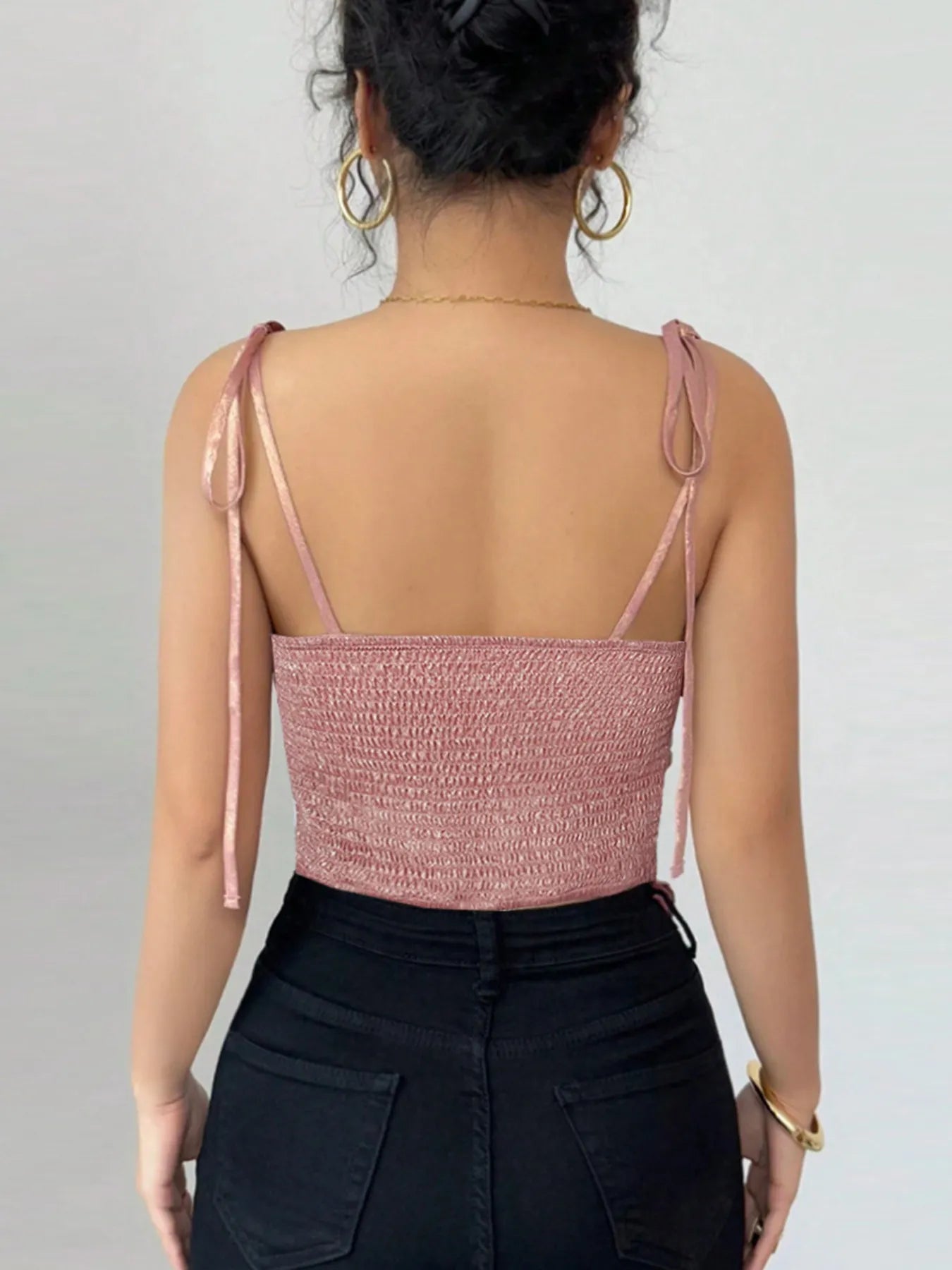 Person wearing a pink crop top with thin straps on a plain background