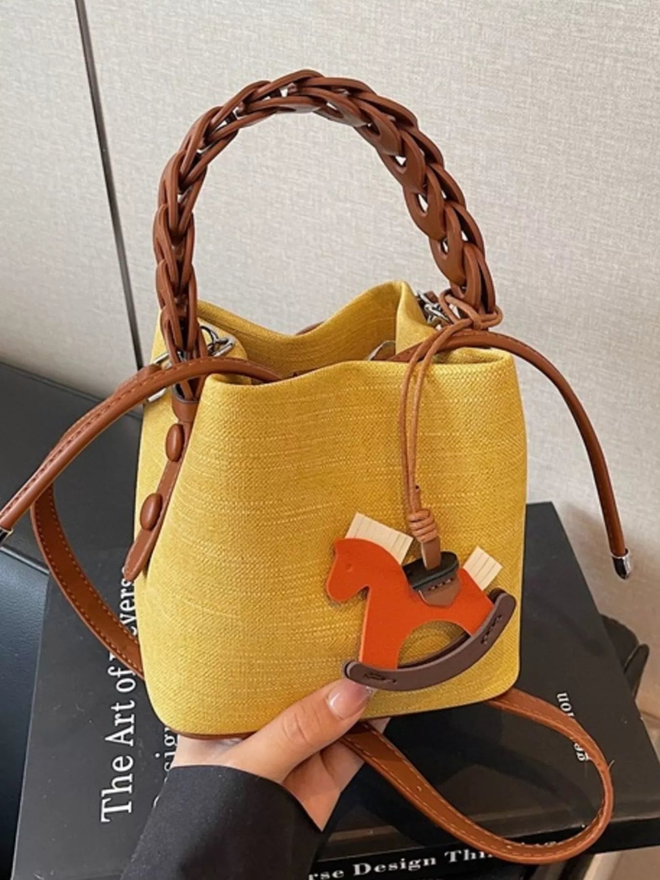 Yellow handbag with brown handle and strap held by a hand on a dark surface.
