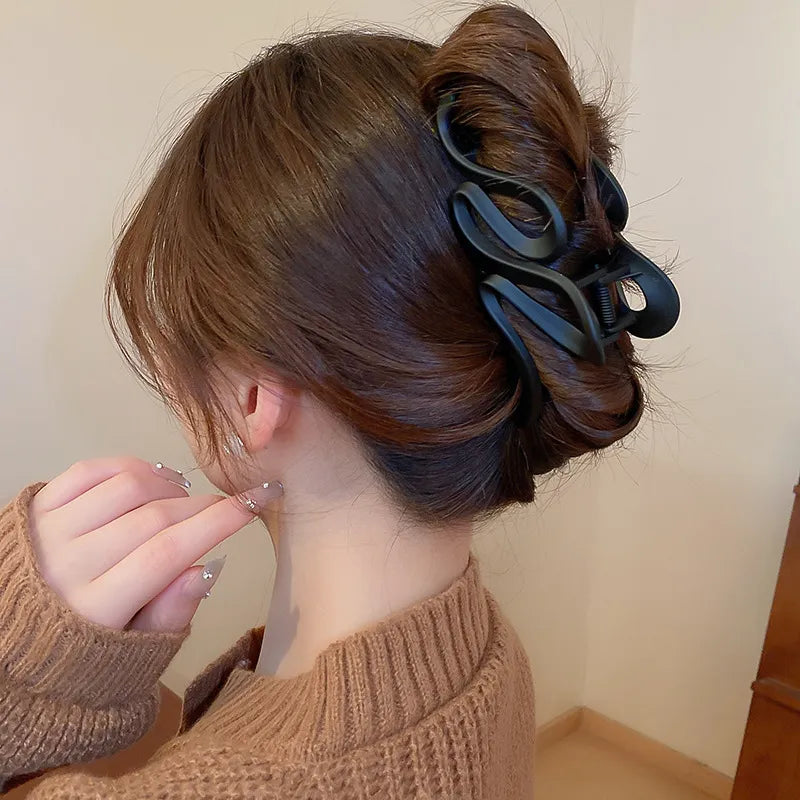 Person with brown hair styled in a bun using a black hair clip against a plain background