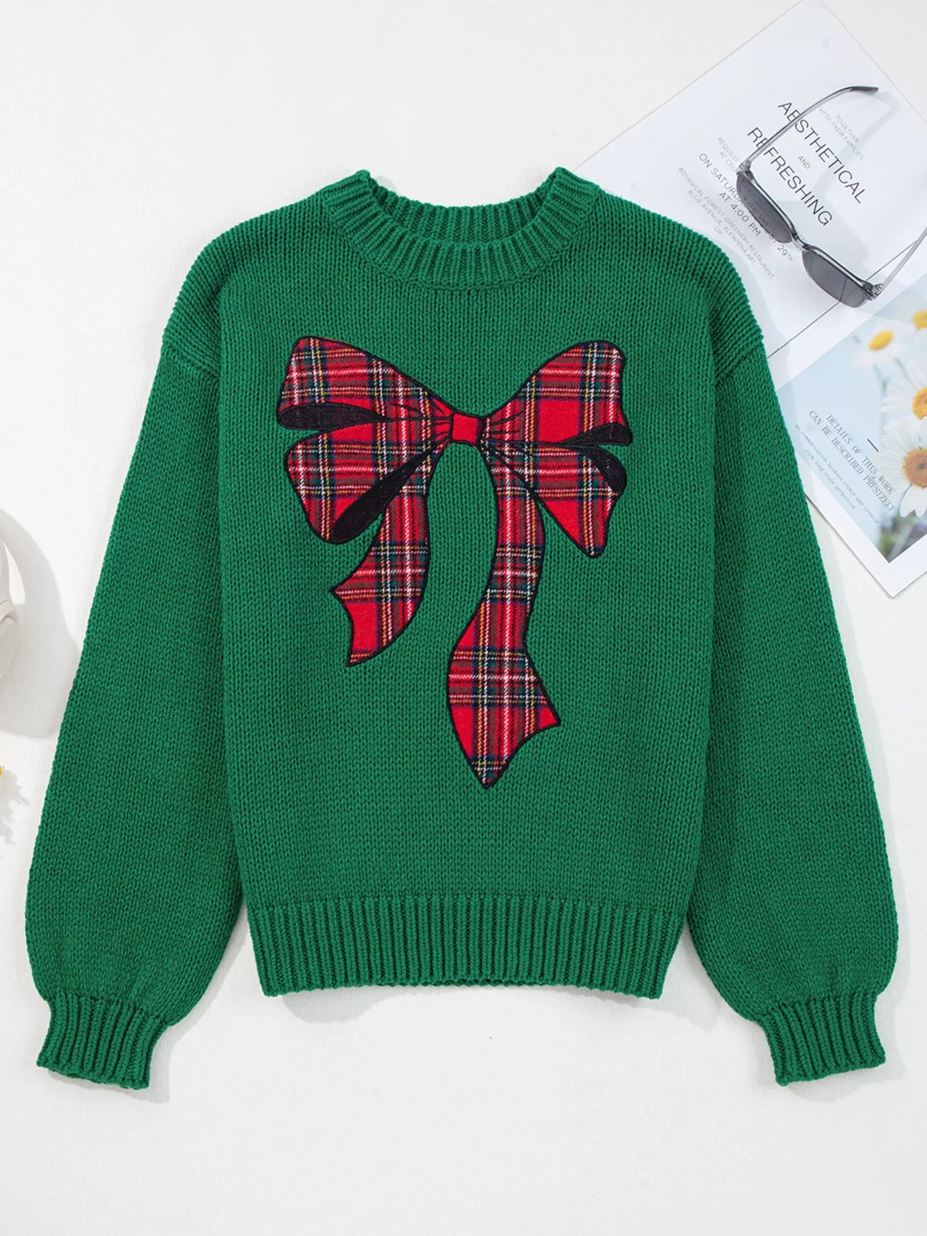 Green sweater with a large plaid bow design on a white background