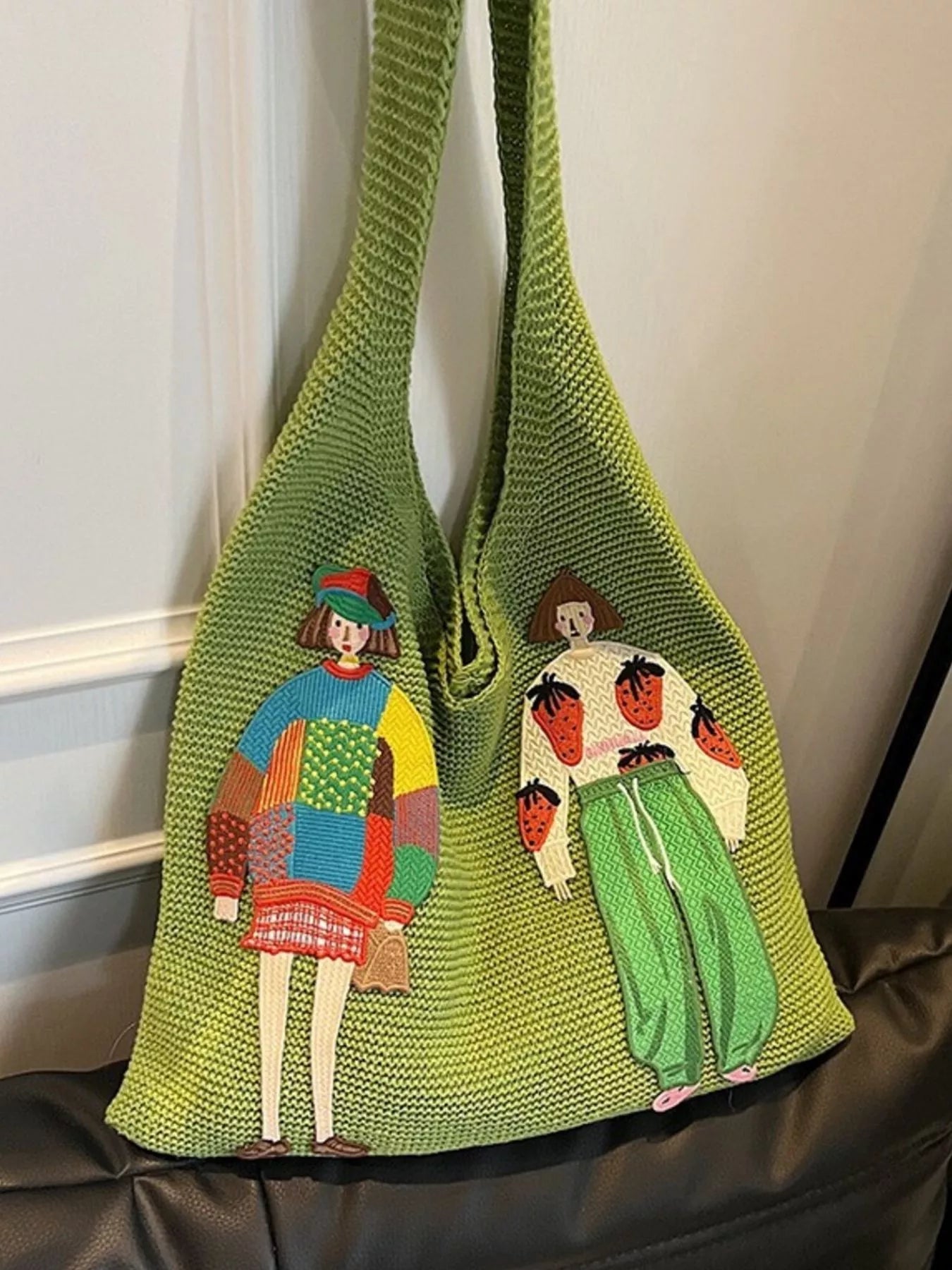 Green knitted bag with embroidered designs of people on a white background