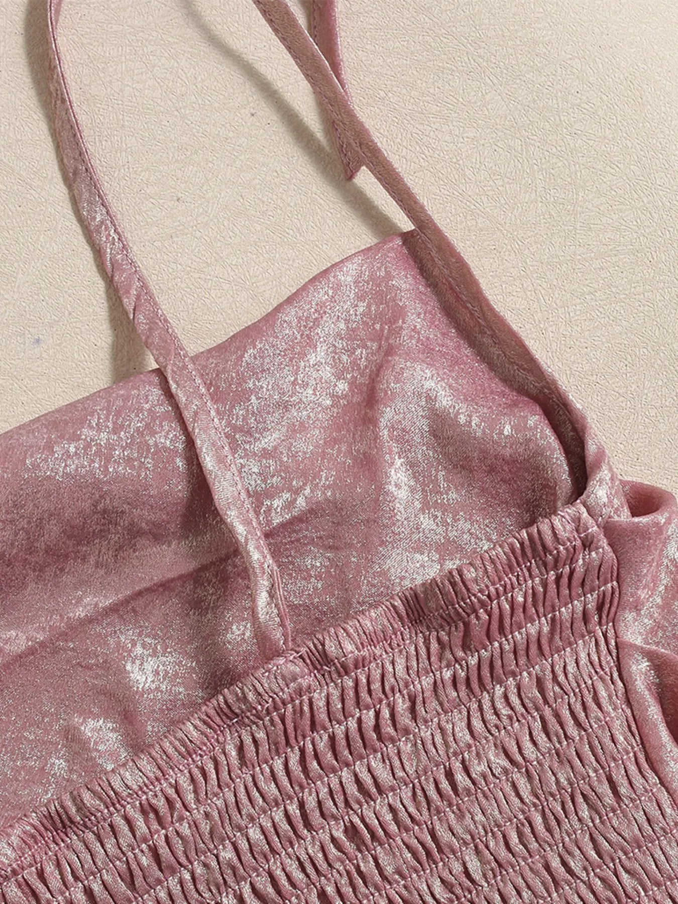 Close-up of a pink textured top with thin straps on a beige background