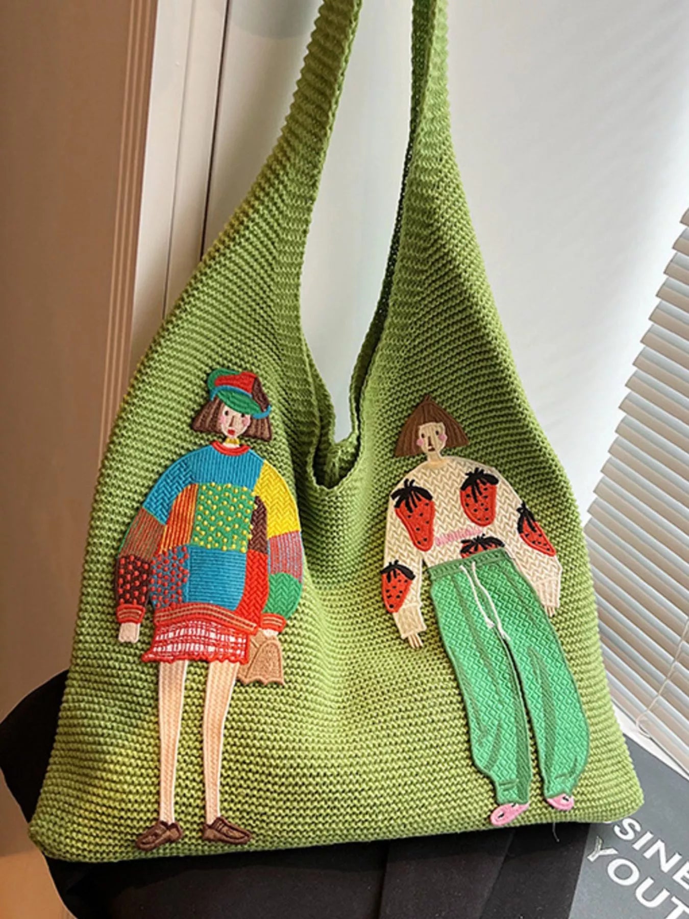 Green knitted bag with embroidered figures on a neutral background