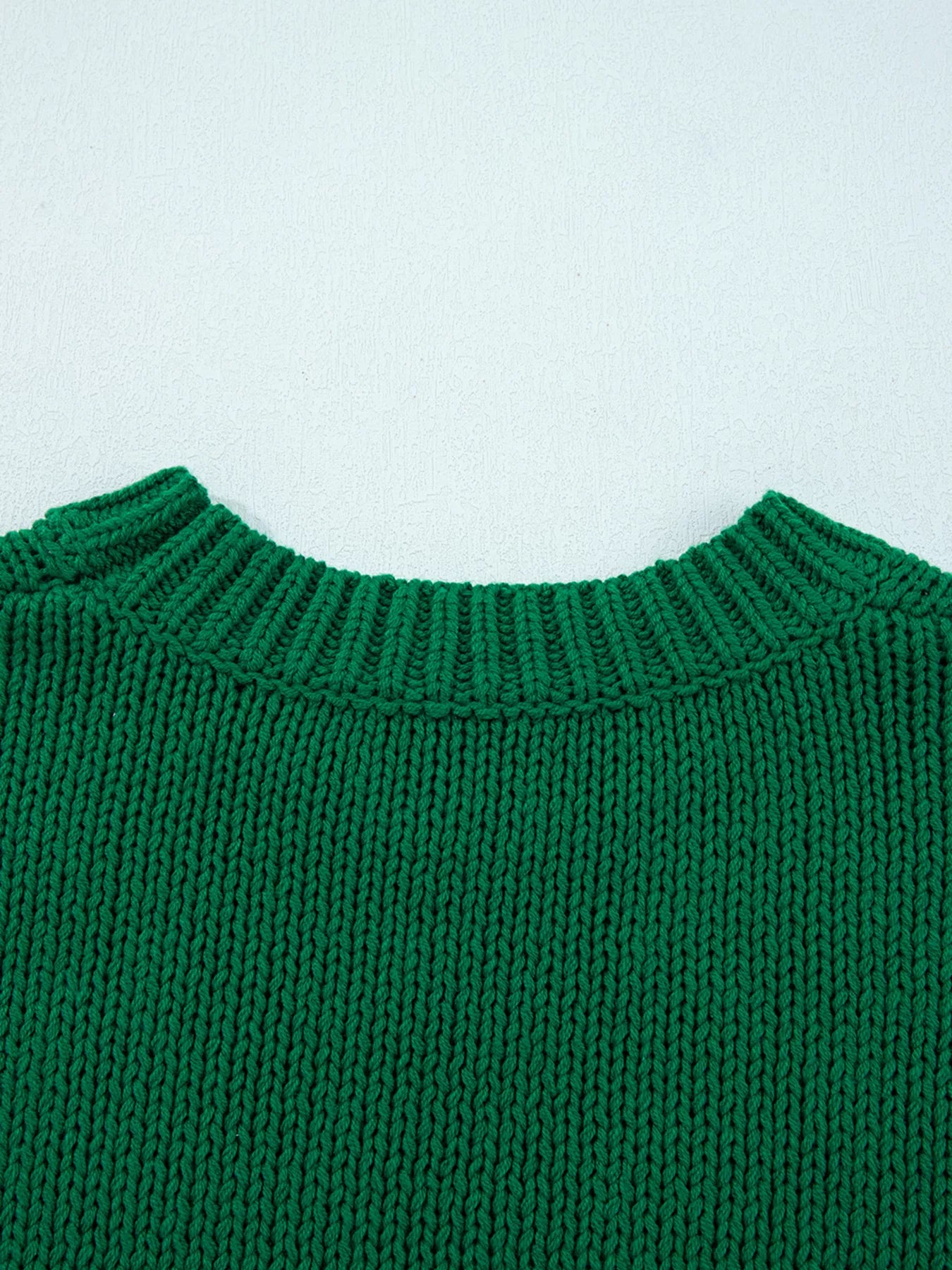 Close-up of a green knitted sweater collar on a light blue background