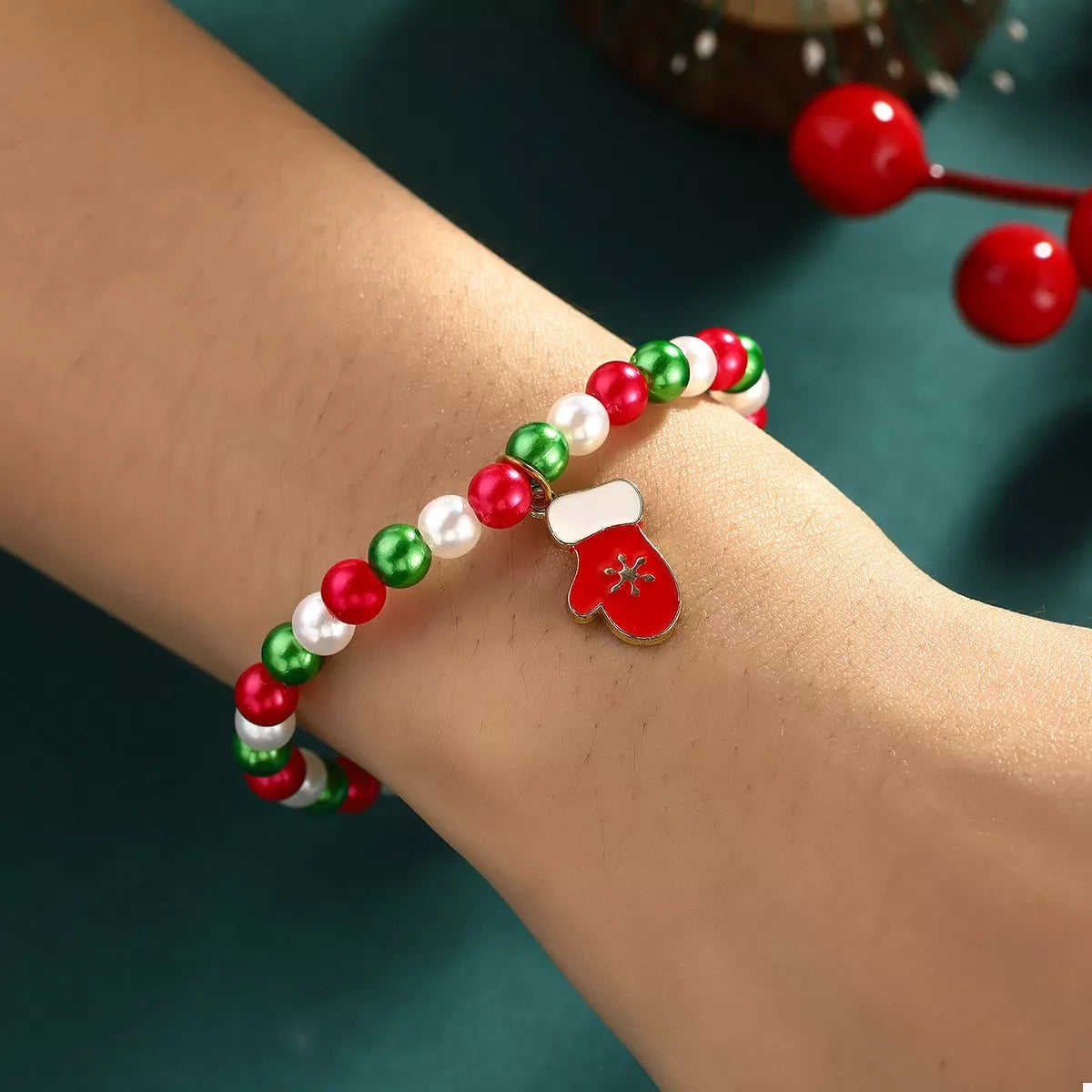 Beaded bracelet with a red mitten charm on a wrist against a teal background