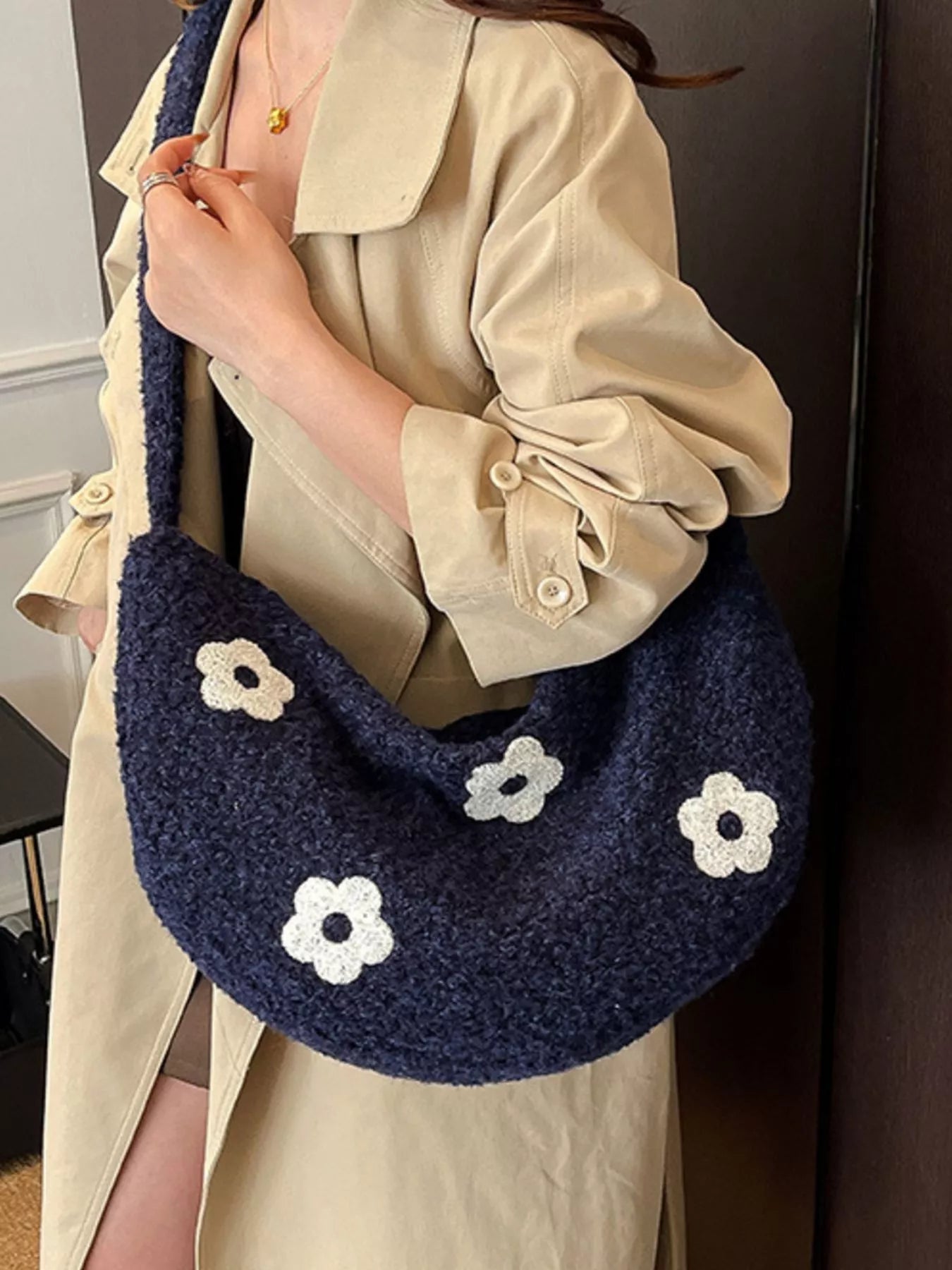 Person holding a navy blue handbag with white flower patterns, wearing a beige coat.