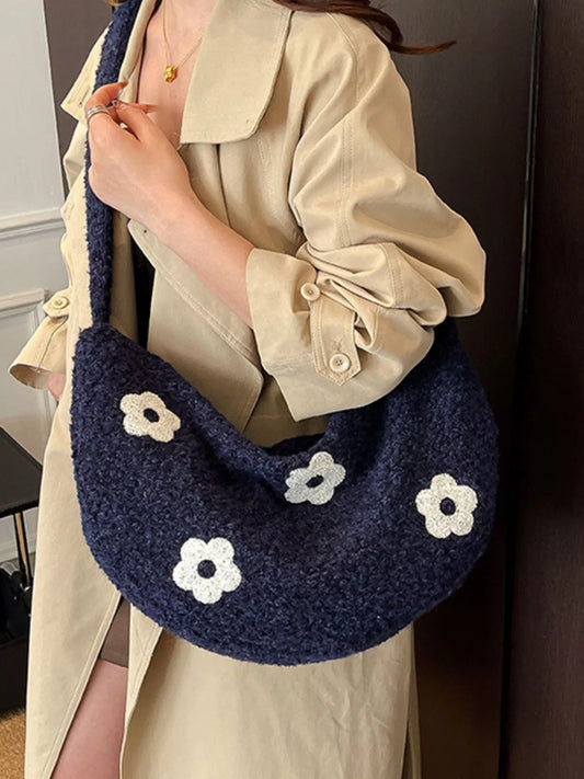 Person holding a navy blue handbag with white flower patterns, wearing a beige coat.
