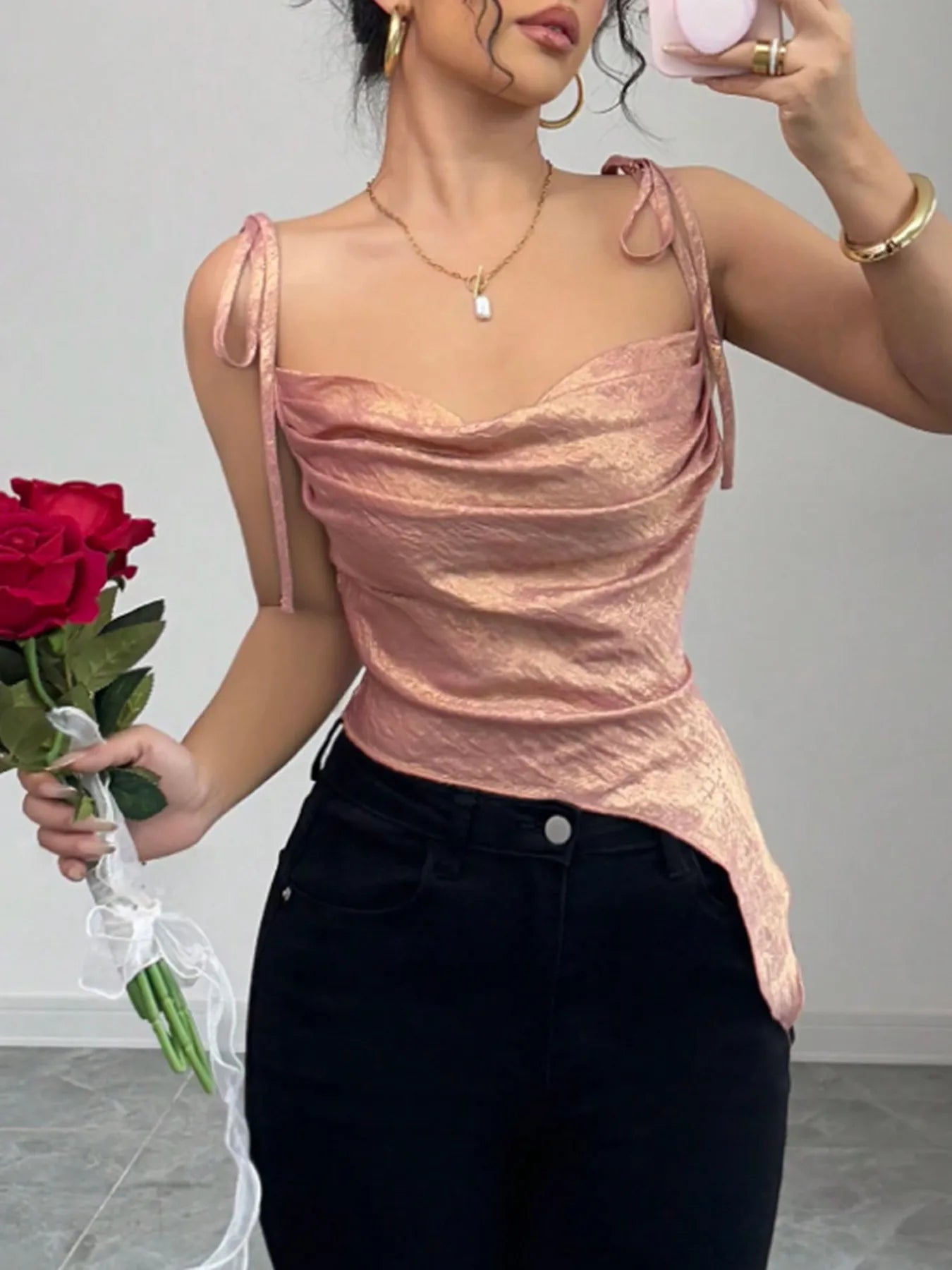 Woman wearing a pink top and black pants, holding a red rose.