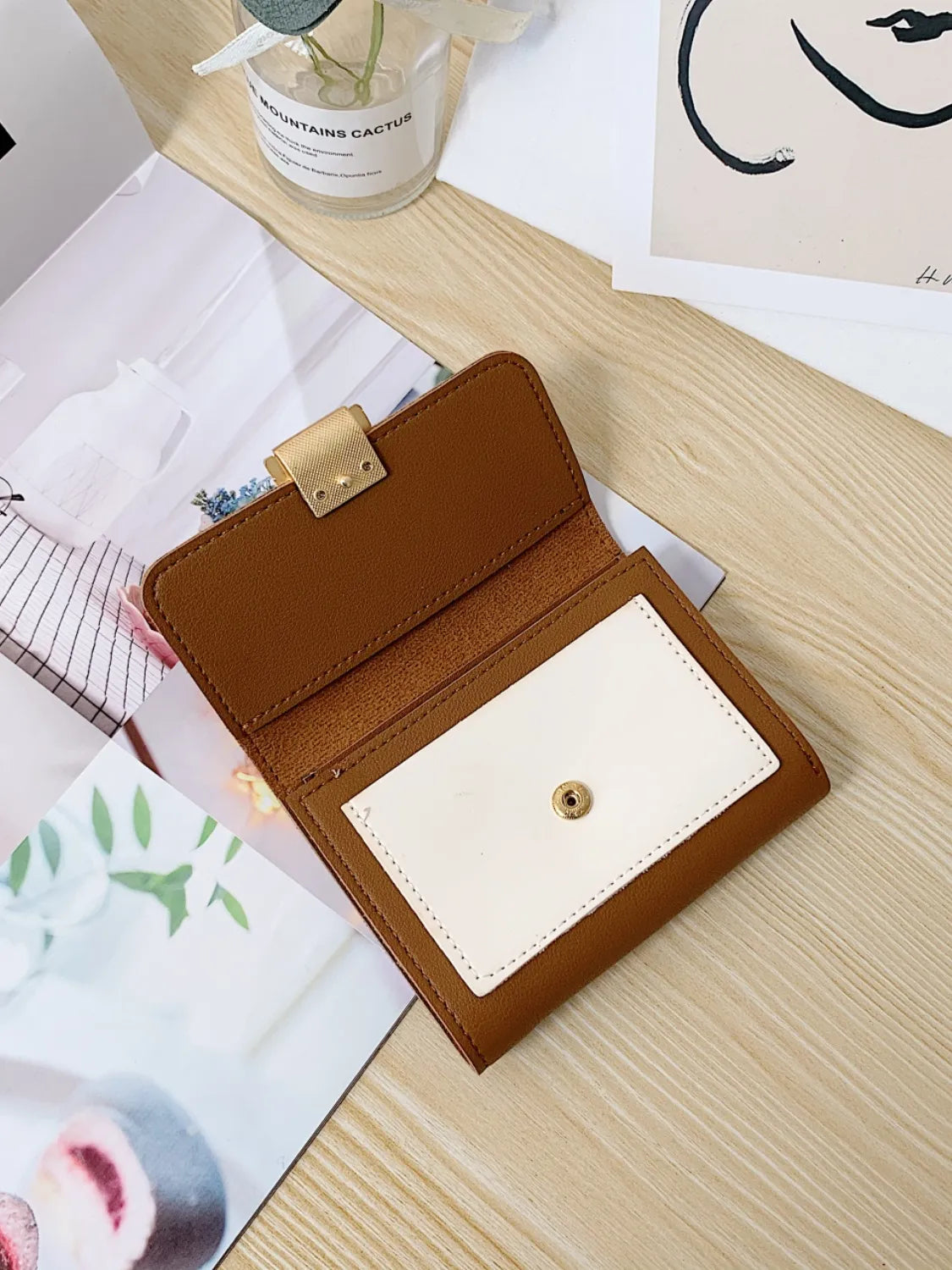 Brown leather wallet with gold clasp on a wooden surface