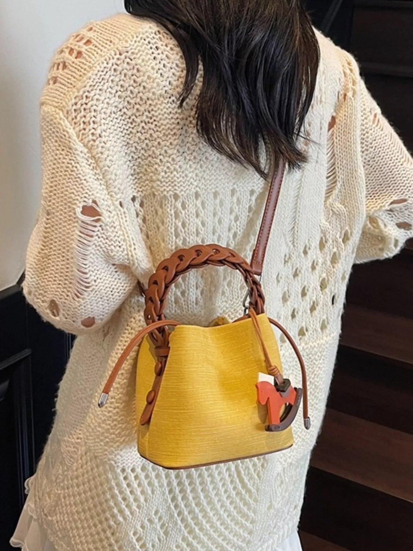 Person wearing a beige knit sweater with a yellow handbag featuring a brown handle.