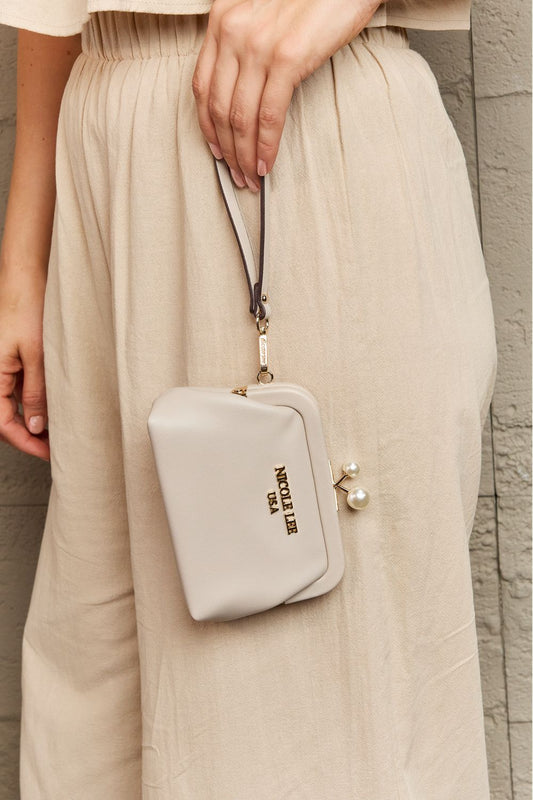 Beige handbag held by a person wearing a beige outfit against a stone wall.