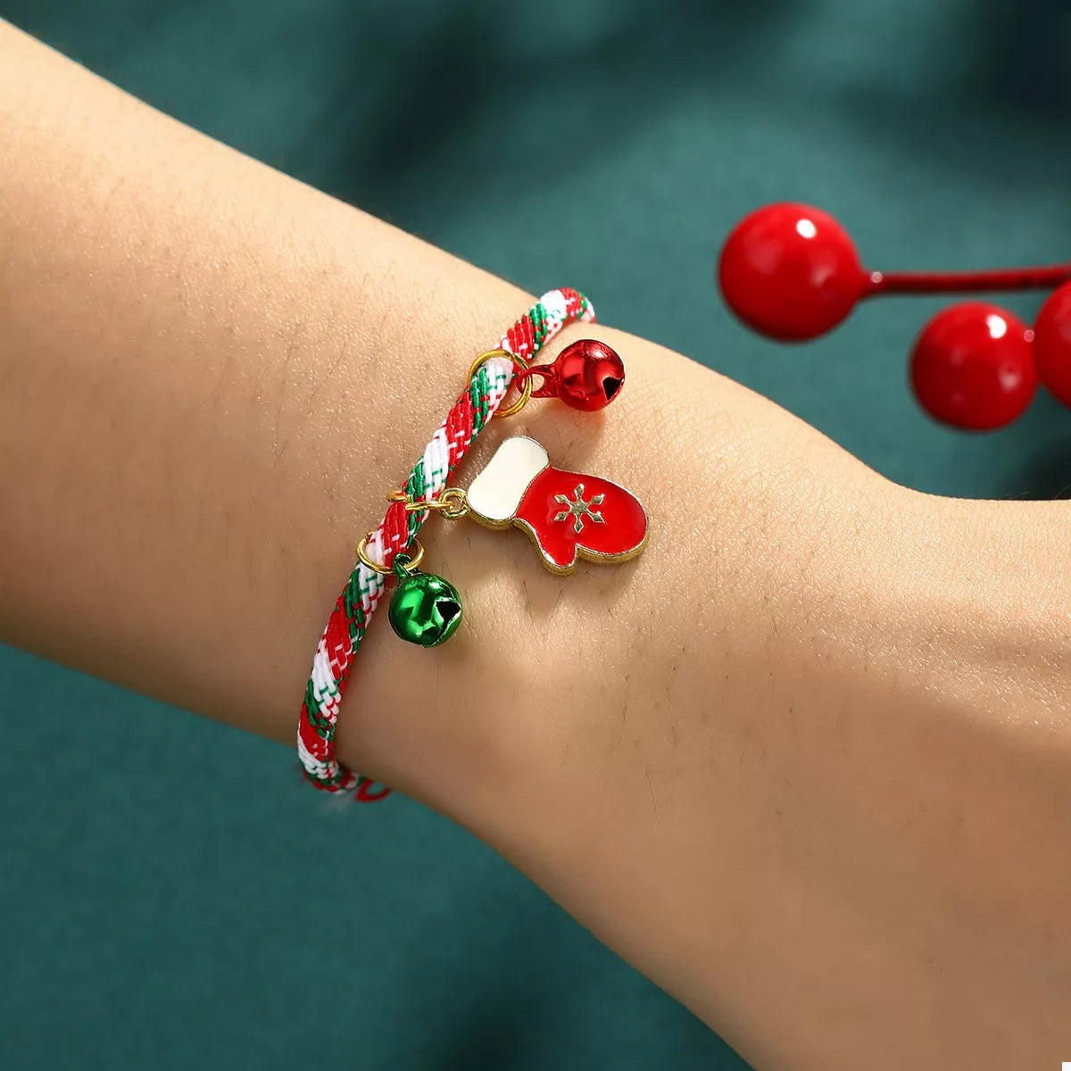 Colorful bracelet with red bell charm on wrist against a teal background