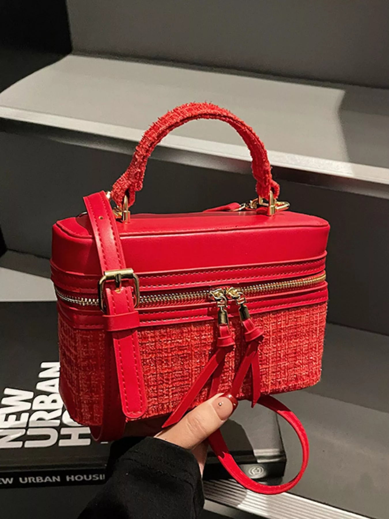 Red textured handbag with gold accents held by a person against a dark background.