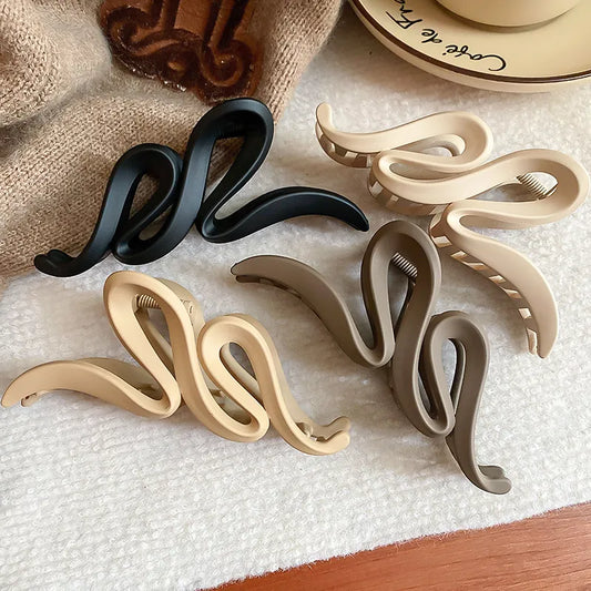 Set of snake-shaped hair clips in black, beige, and gray on a textured surface.