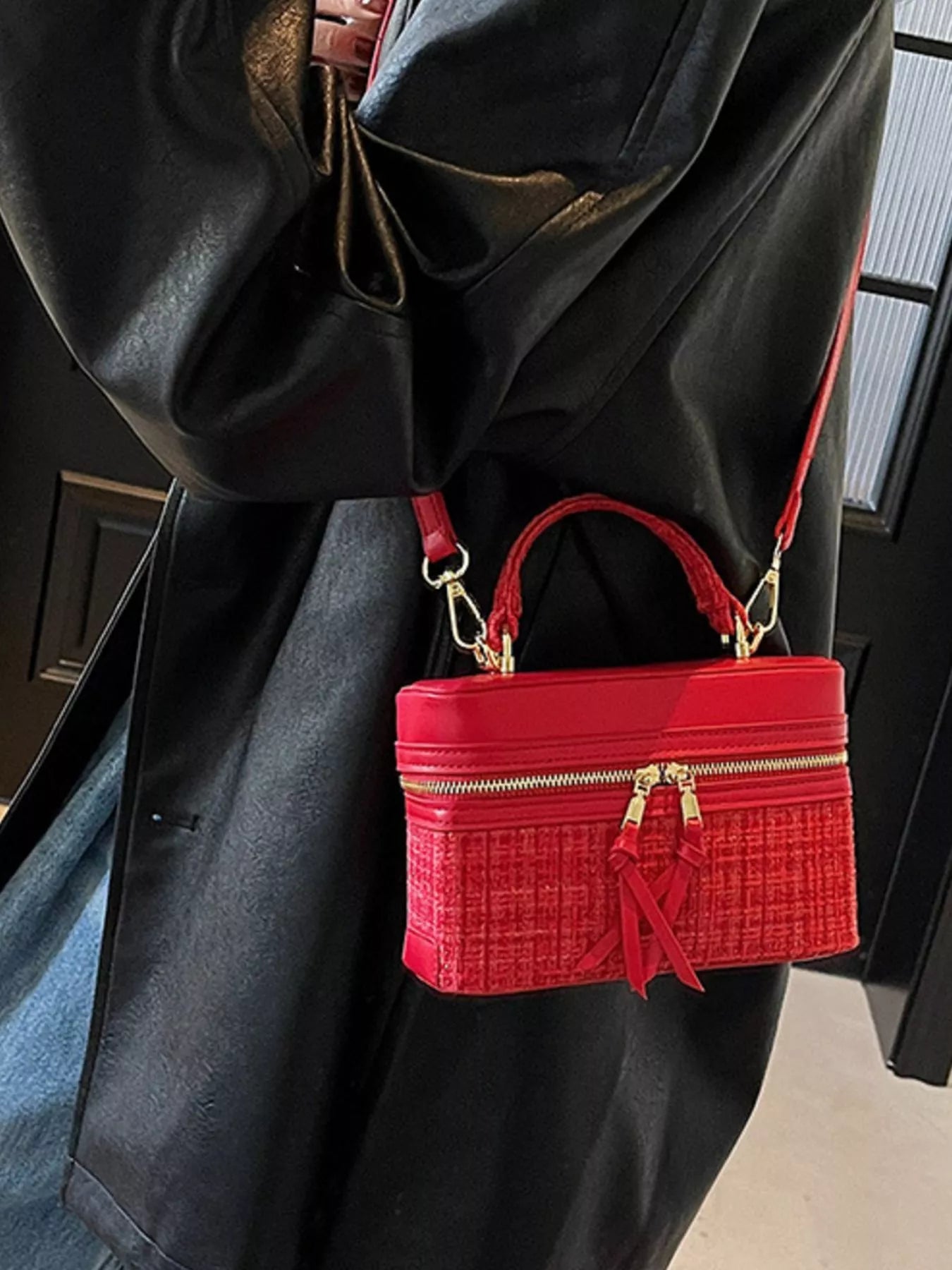 Red handbag with gold accents worn over a black coat
