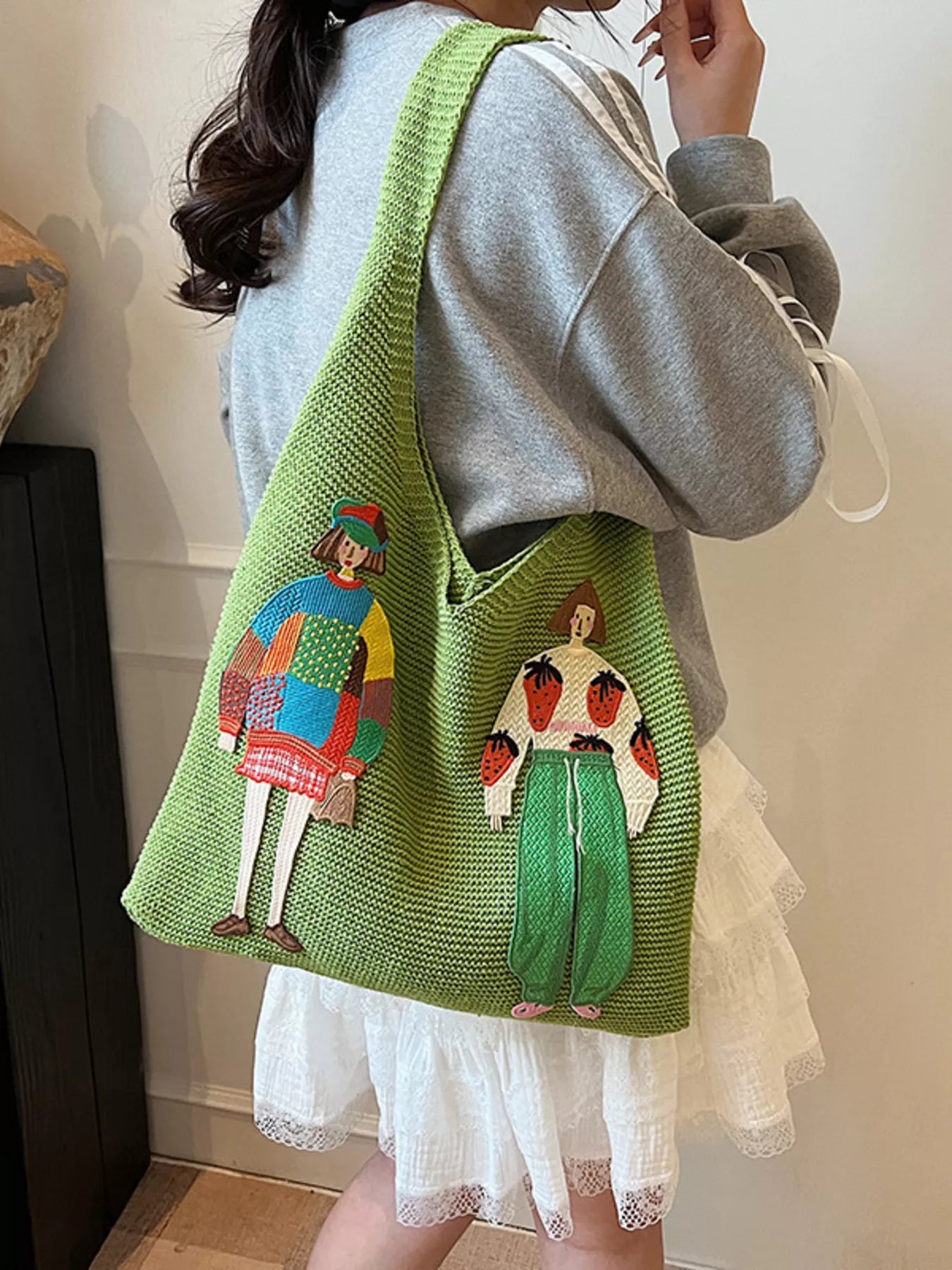 Green knitted bag with embroidered designs worn by a person indoors.