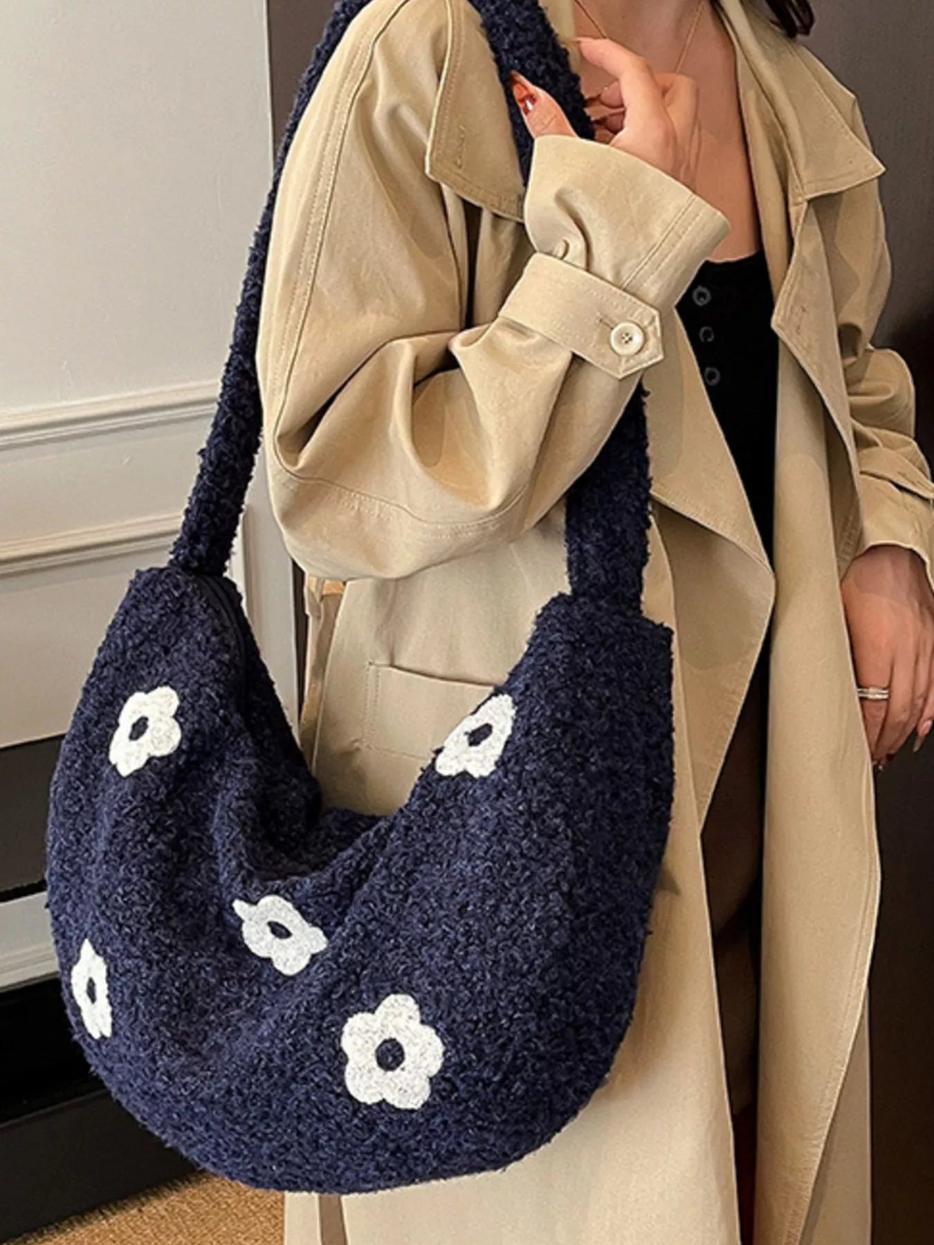 Navy blue handbag with white floral patterns held by a person wearing a beige coat.