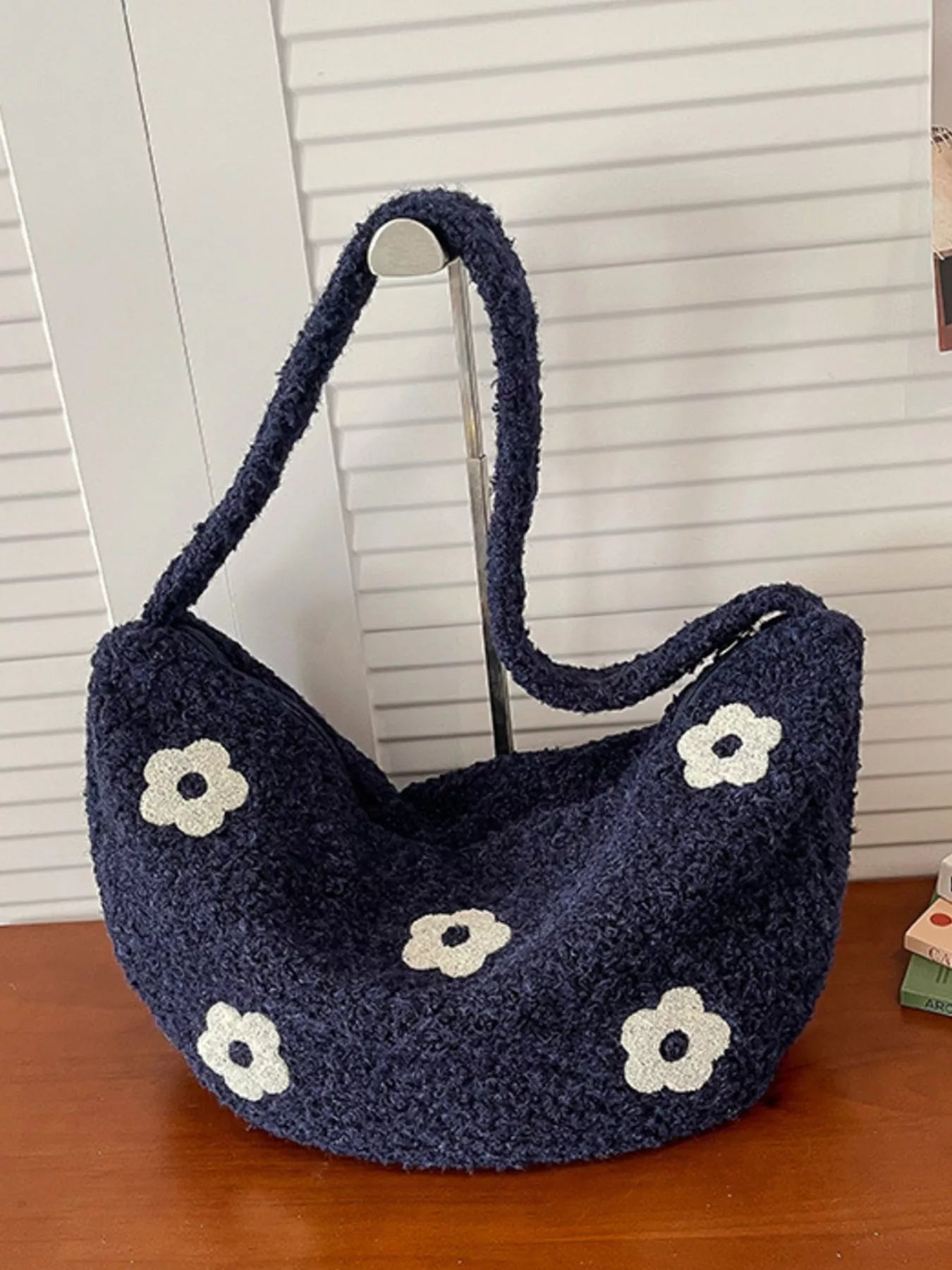 Navy blue handbag with white floral patterns on a wooden surface.