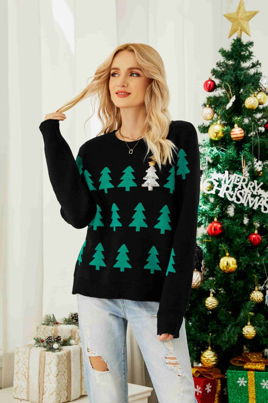 Woman wearing a black sweater with green Christmas tree patterns in front of a decorated Christmas tree.