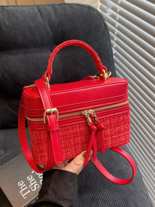 Red handbag with gold accents held by a person, with a blurred background