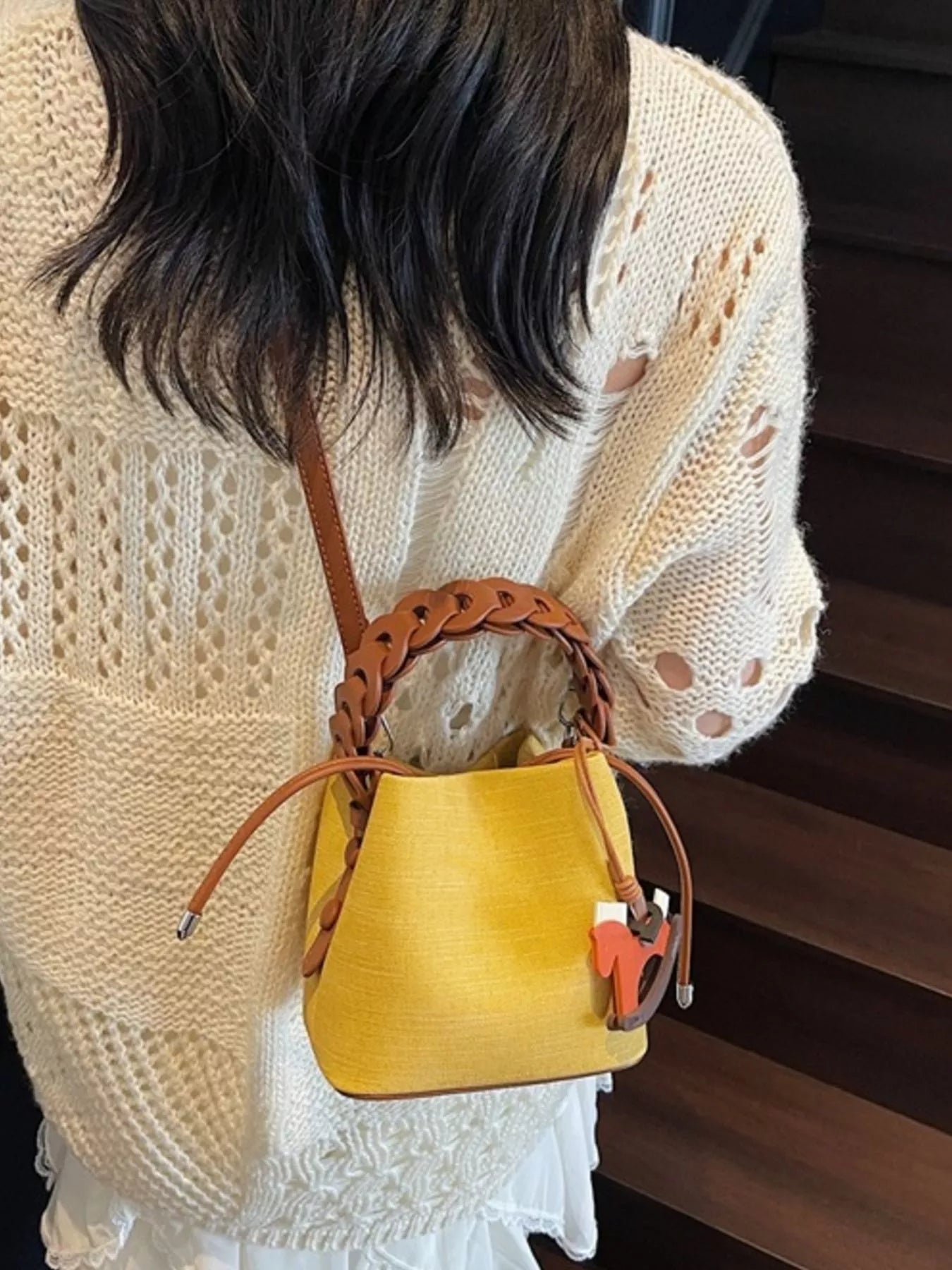 Person wearing a yellow bucket bag with a brown strap.