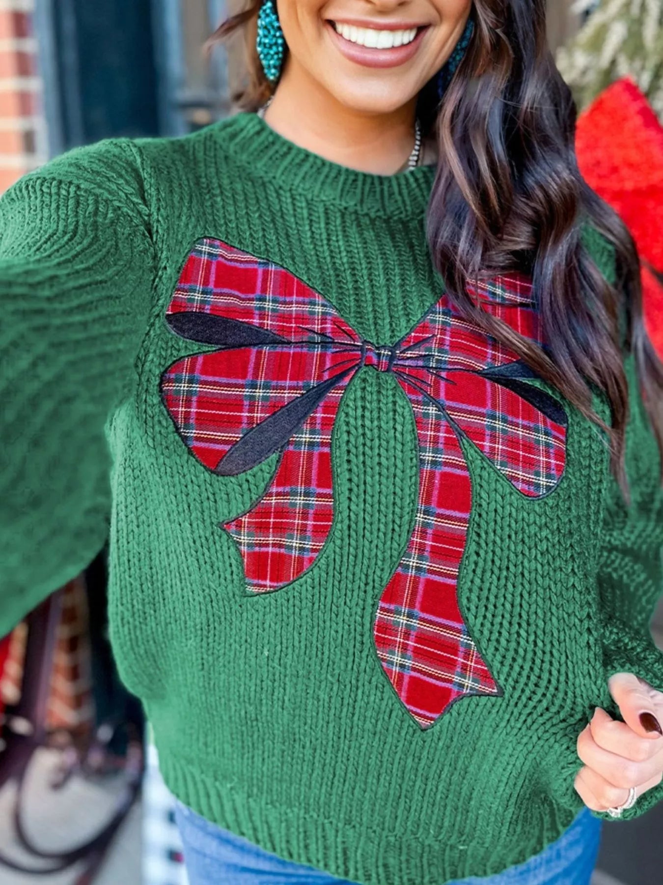 Green sweater with a large red plaid bow worn by a person.